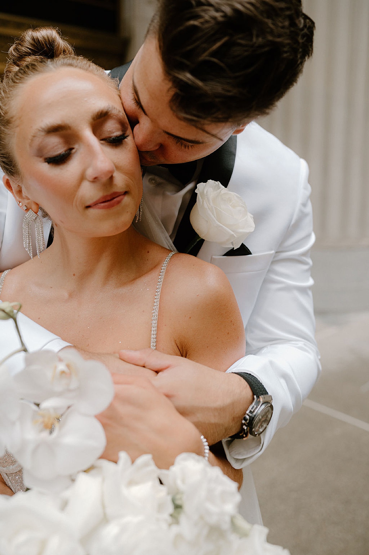 groom in white evening jacket kisses bride with orchid bouquet during Glitz & Glam Chicago Wedding