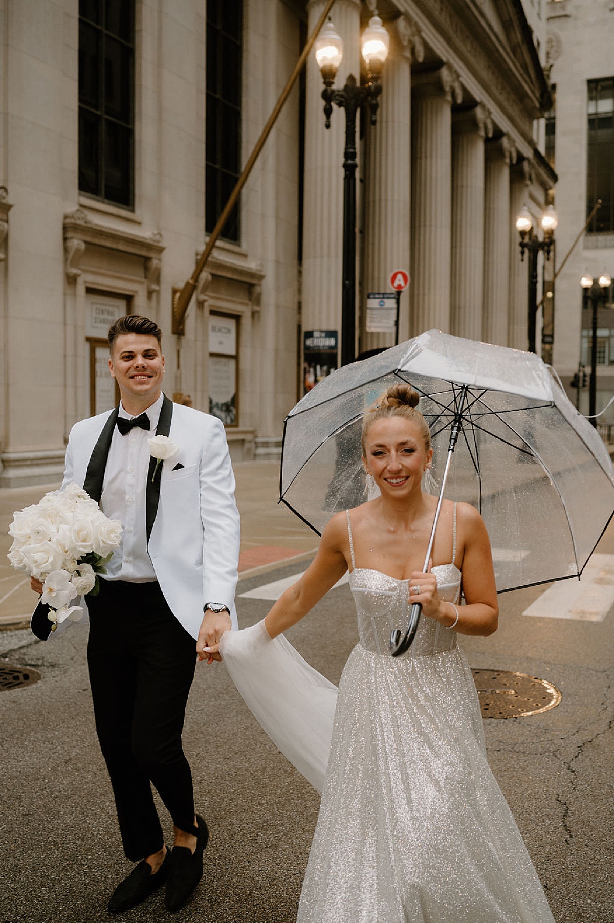 bride carries clear umbrella while groom holds rose and orchid bouquet before Glitz & Glam Chicago Wedding