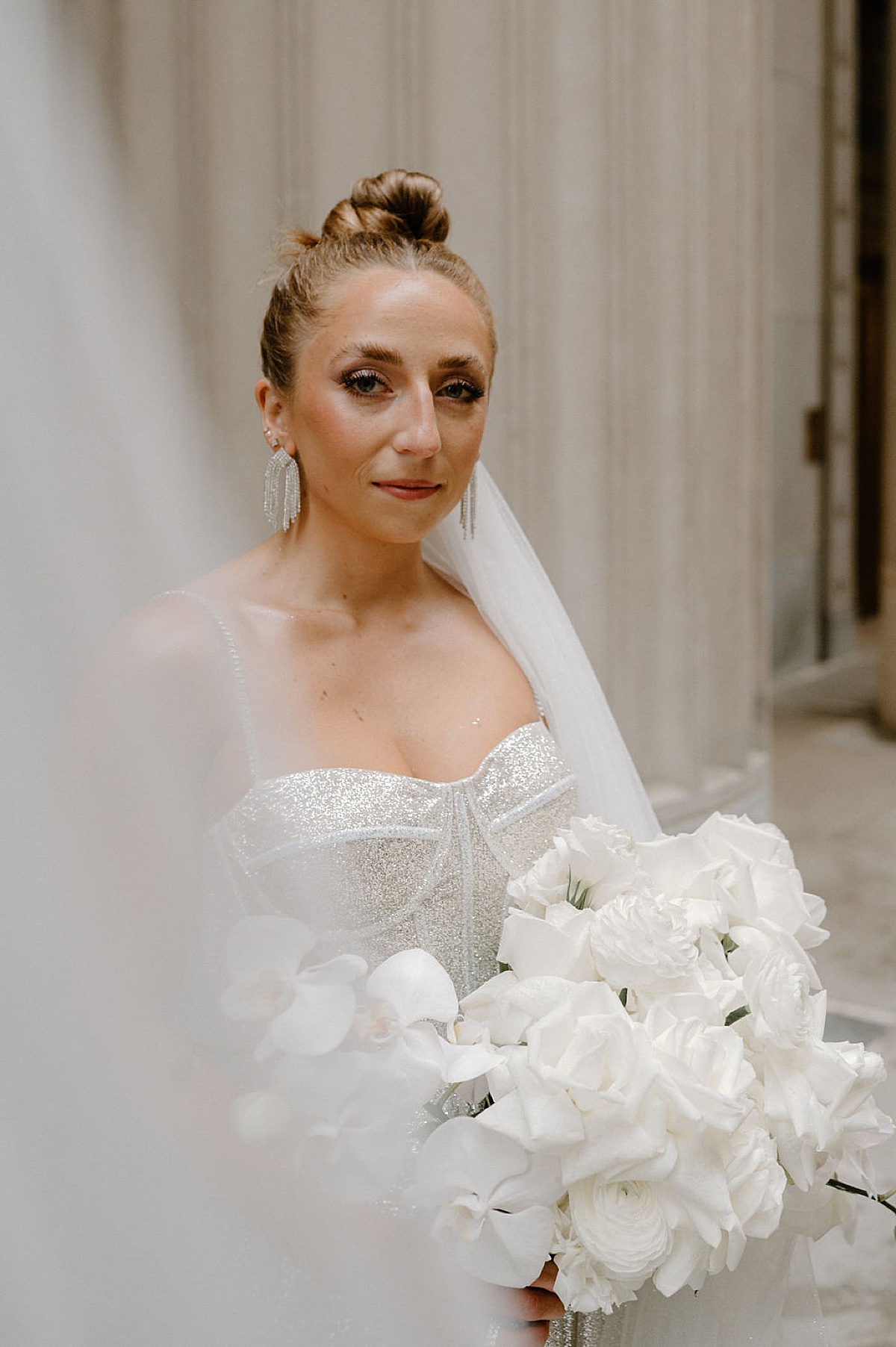 bride with diamond drip earrings and shite rose and orchid bouquet poses for Midwest wedding photographer 