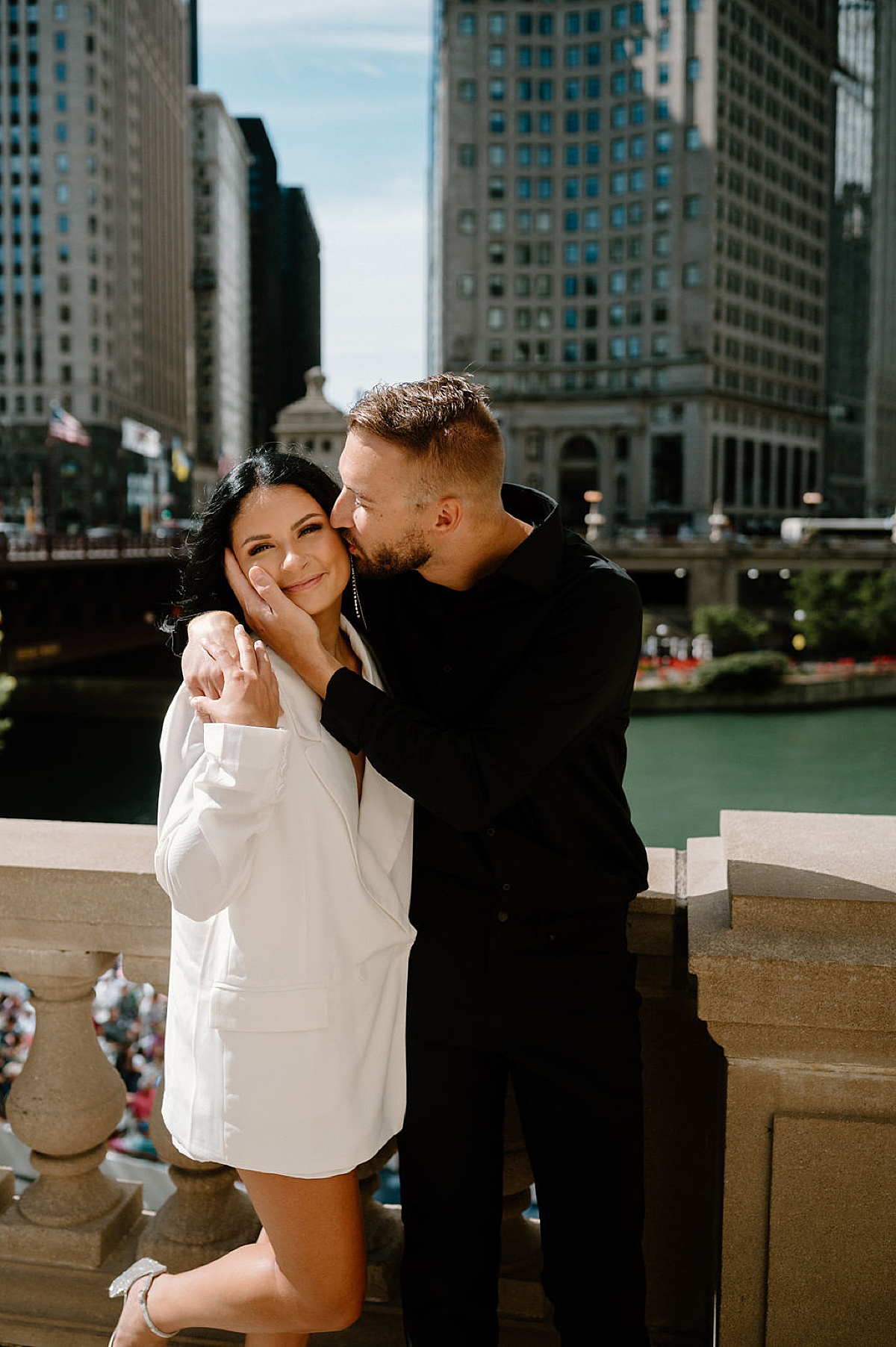 cute couple pose on bridge while he kisses her cheek during big city engagement session