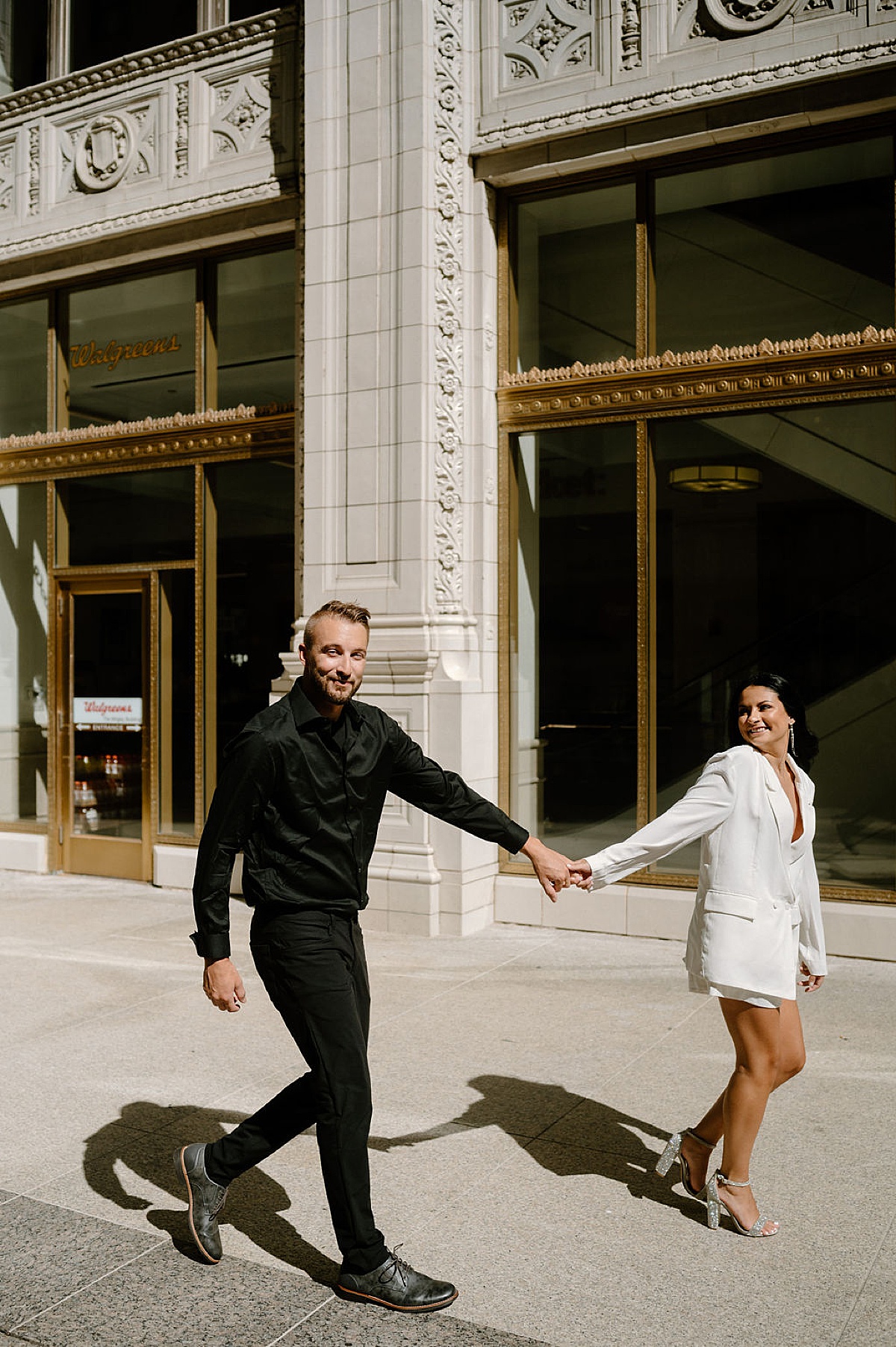 glamorous man and woman in glitter block heels walk through big city engagement session