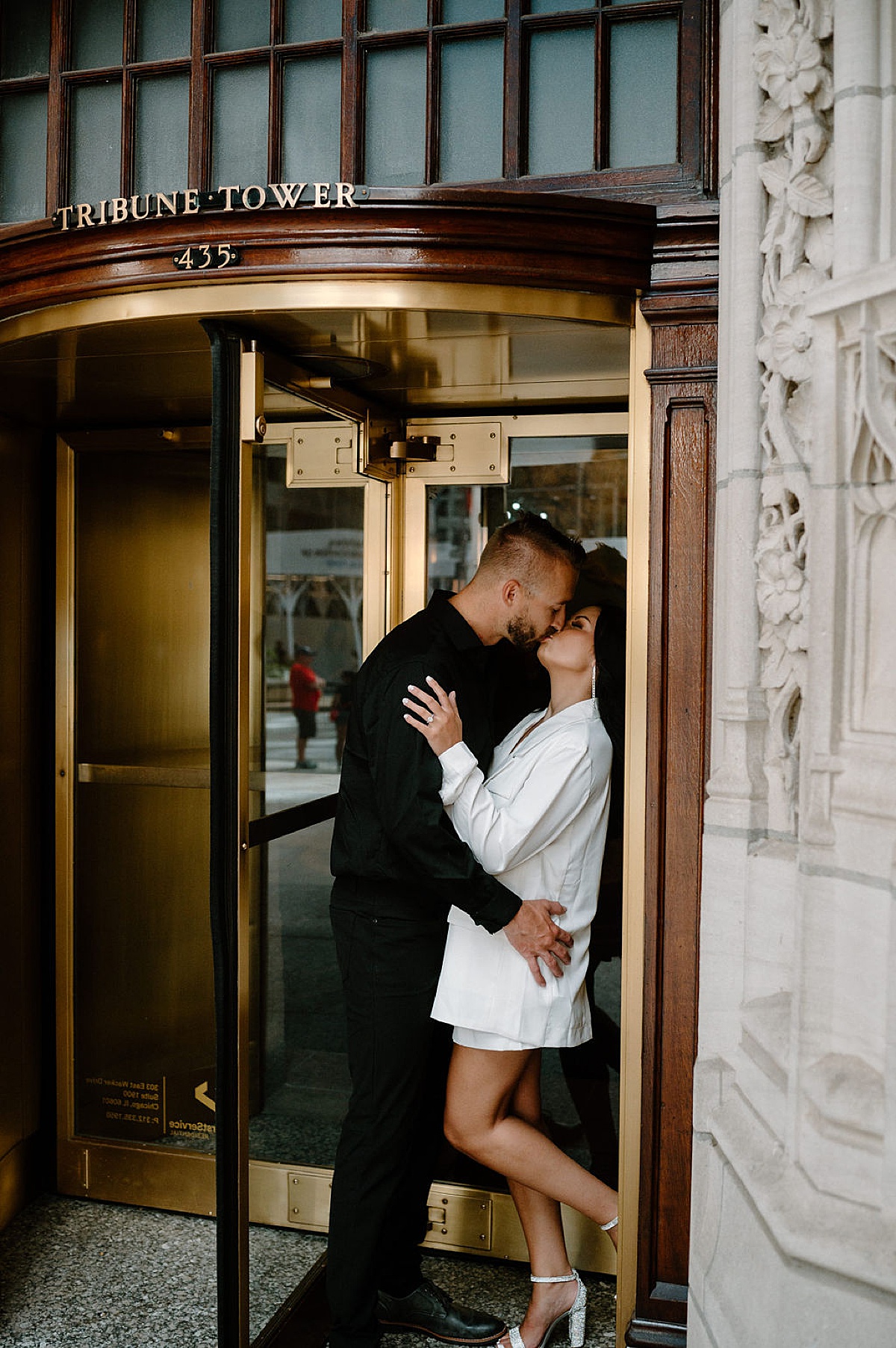 engaged man and woman kiss in gold revolving door during shoot by Chicago wedding photographer
