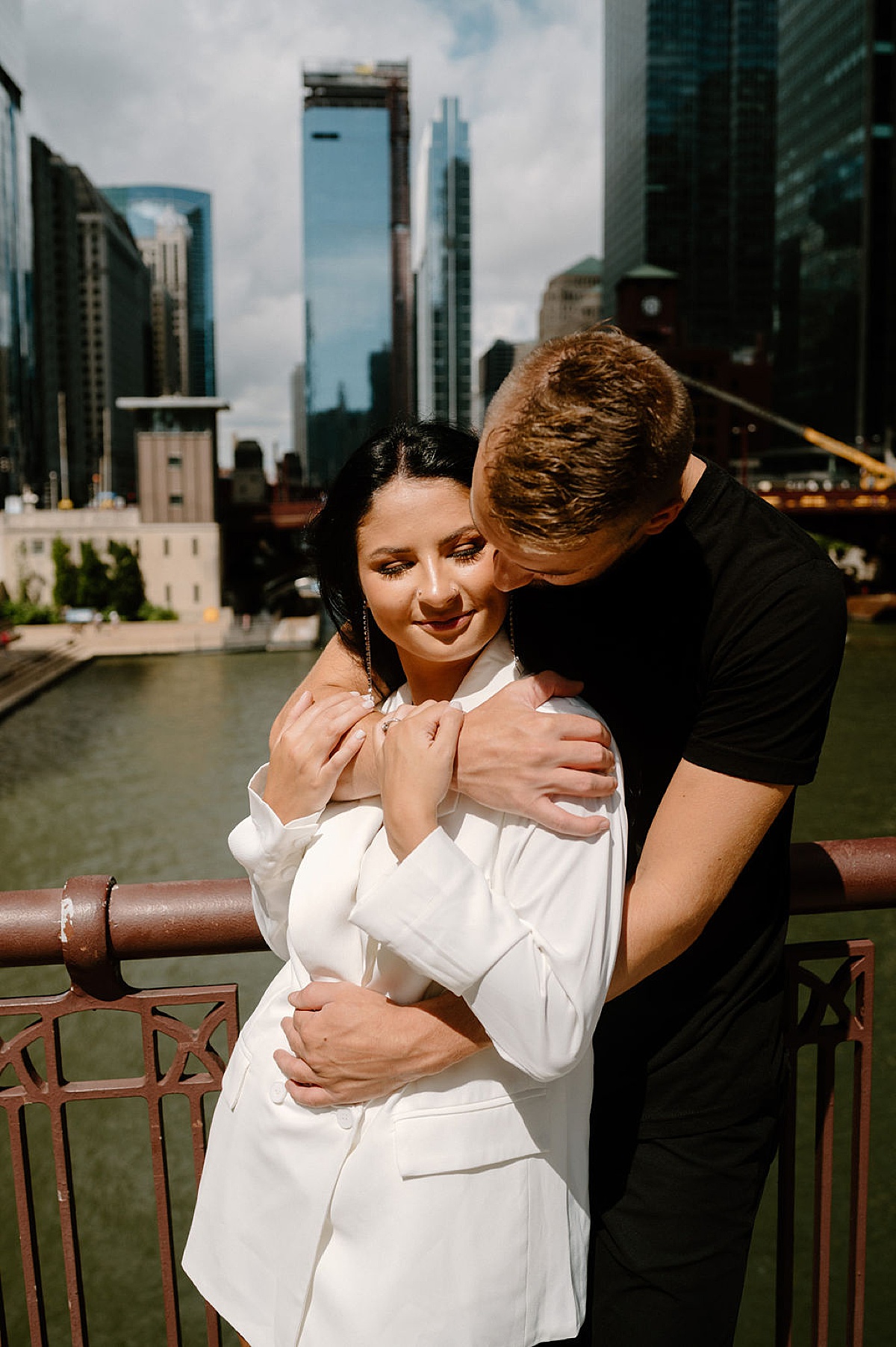 man kisses woman in white blazer by river during session with Chicago wedding photographer