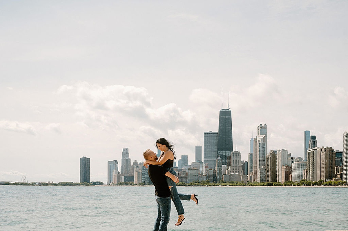 man lifts fiance off the ground in front of Chicago skyline during engagement shoot with Indigo Lace Collective