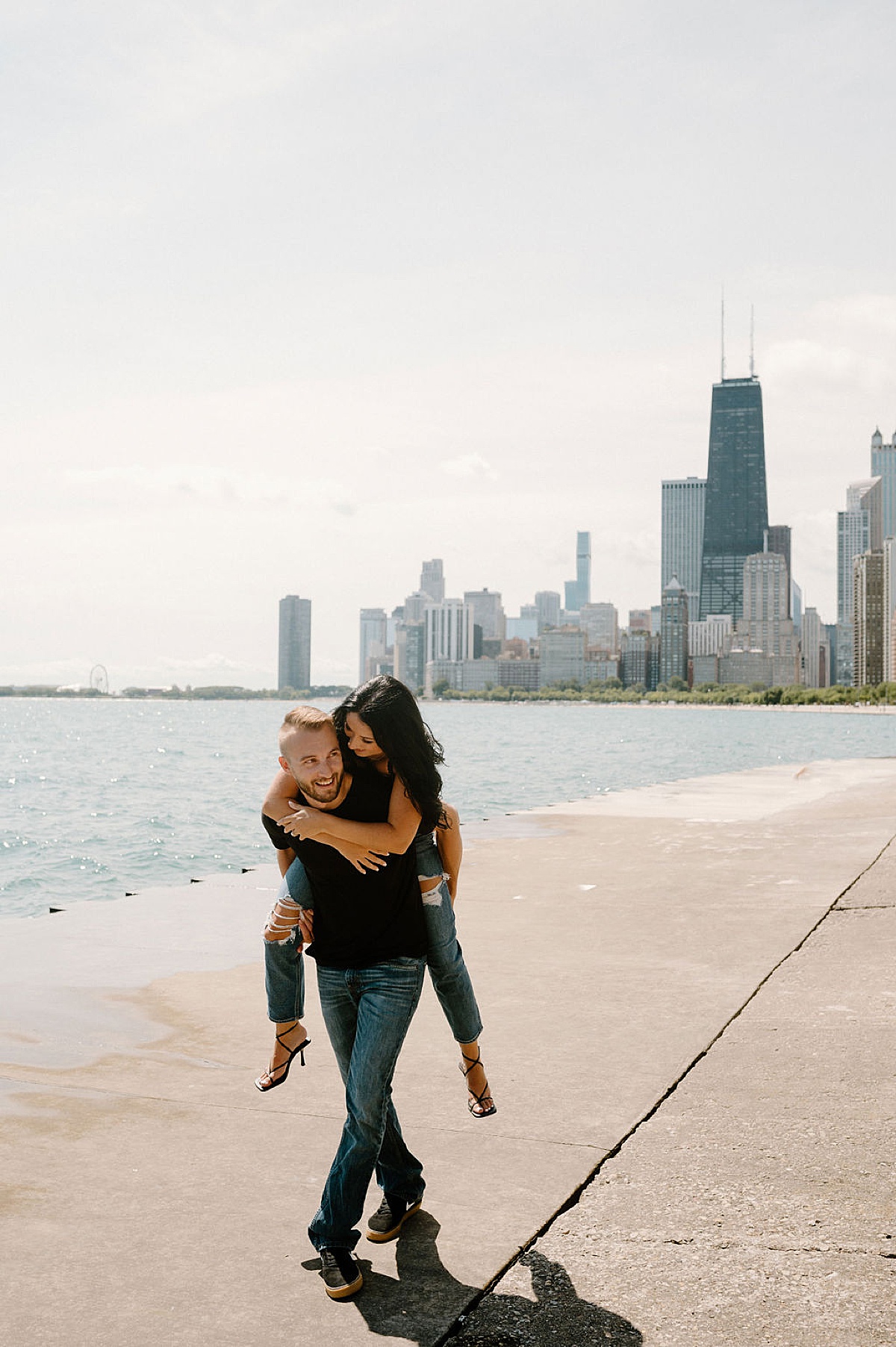 man gives fiance a piggyback ride along waterfront during big city shoot with Indigo Lace Collective