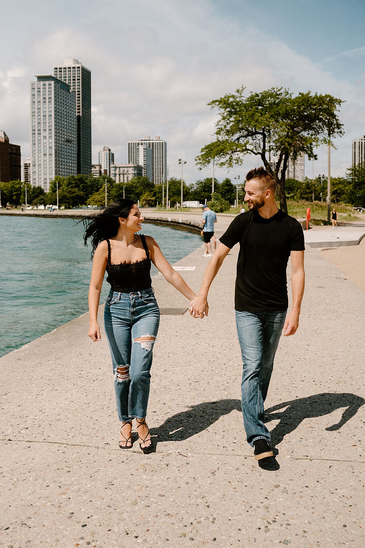 young couple walk along city lake park during romantic engagement shoot with Indigo Lace Collective