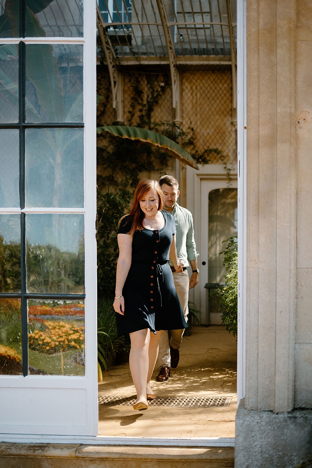 Couple walks hand in hand through charming greenhouse in English countryside during Wrest Park Engagement session