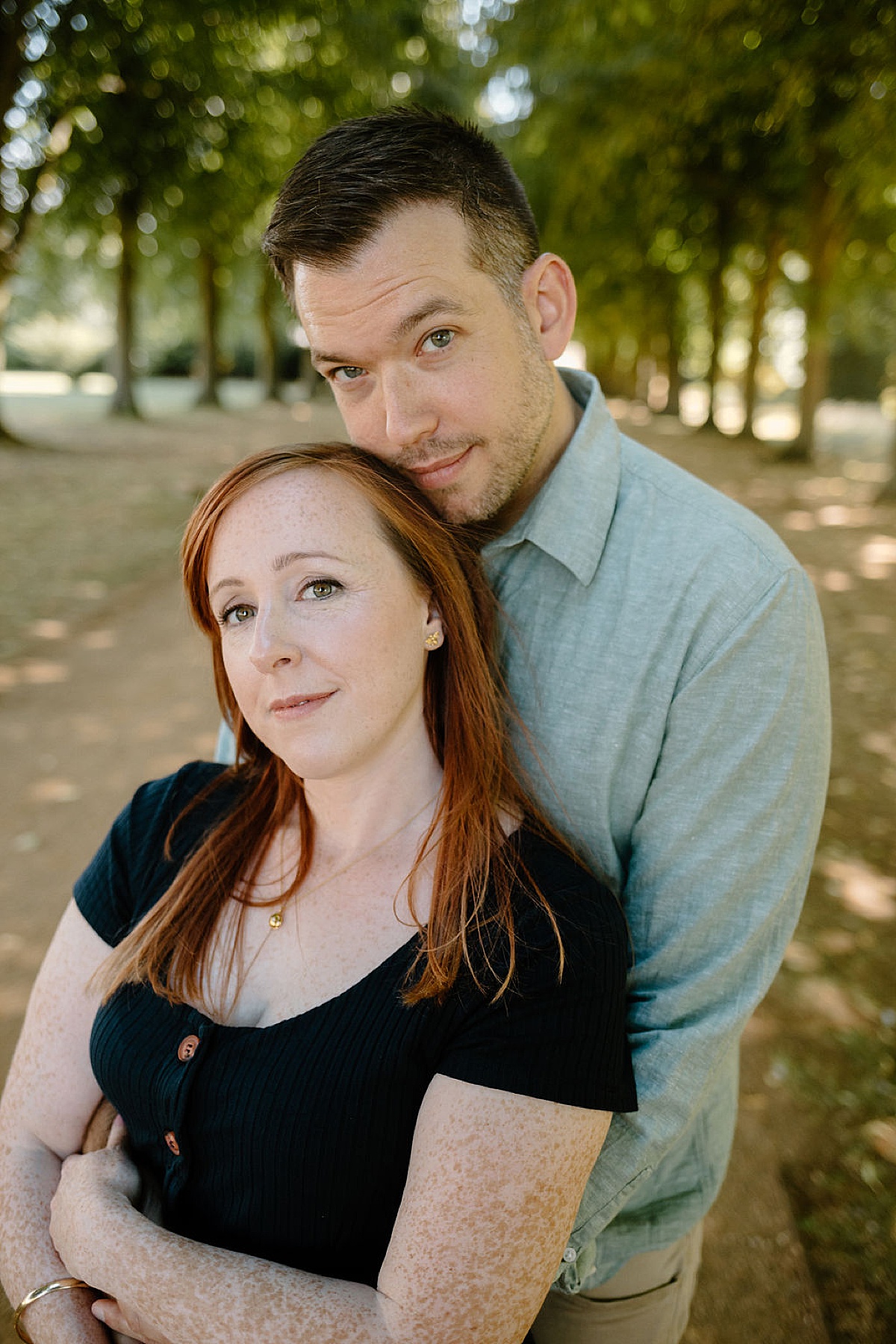 newly engaged couple poses in tree lined avenue during session with Indigo Lace Collective