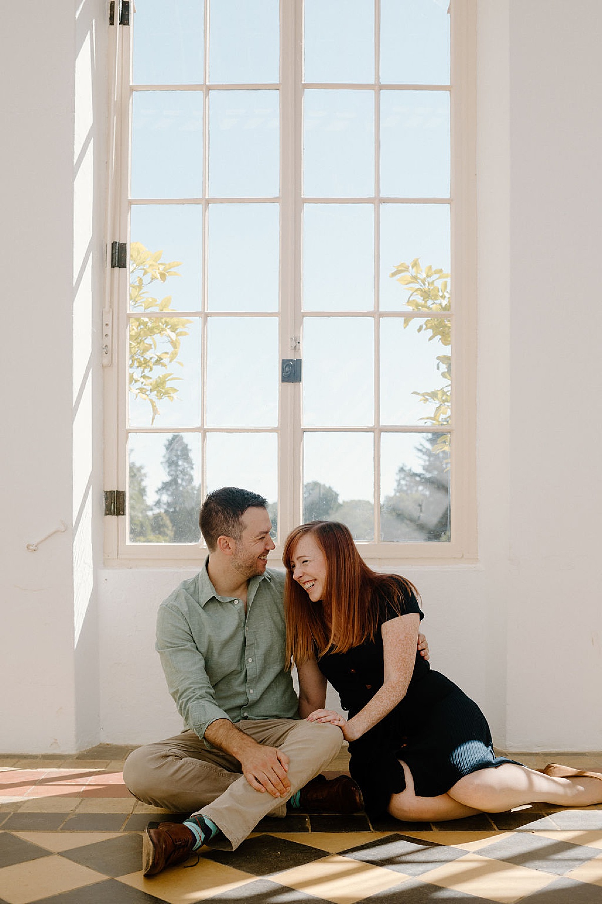 Couple sits on tiled floor laughing during engagement session shot by London Wedding Photographer