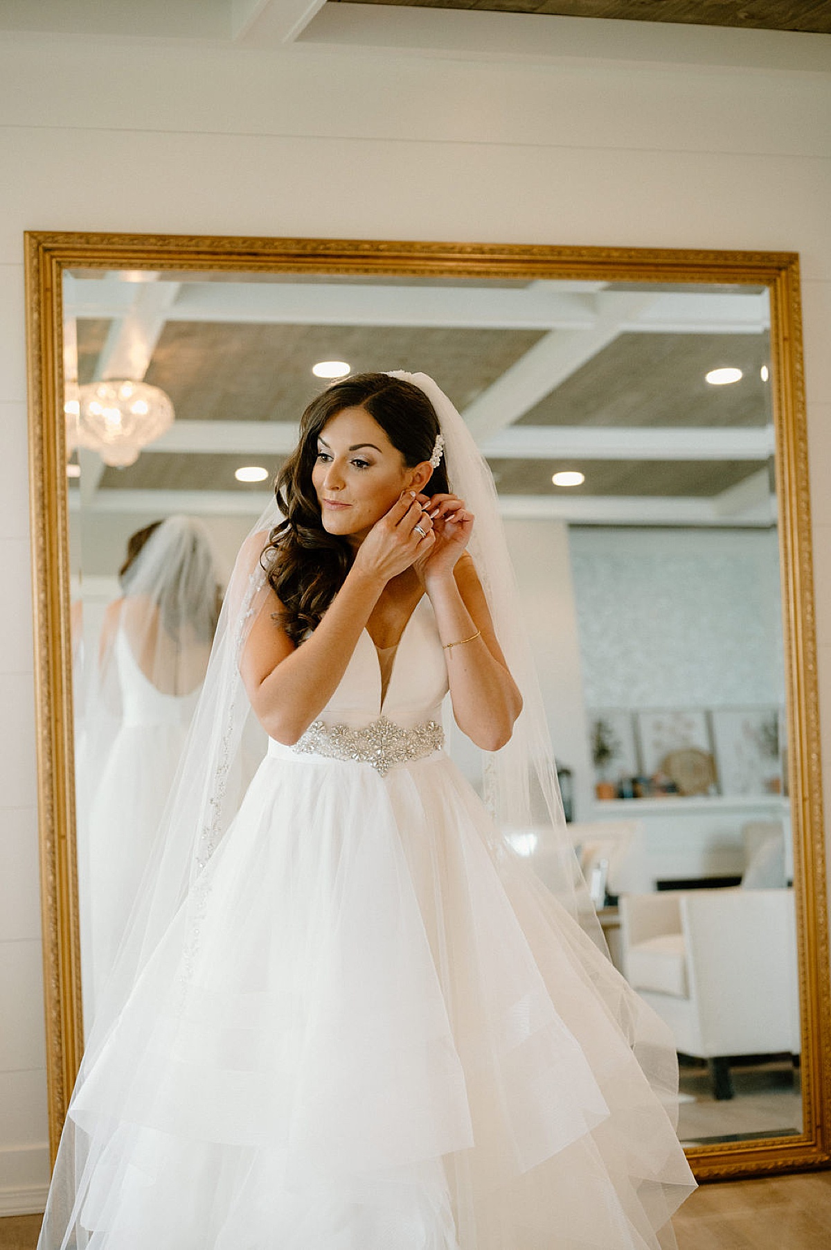 bride in tulle gown with diamond belt fastens earring while getting ready before romantic Etre Farms summer wedding