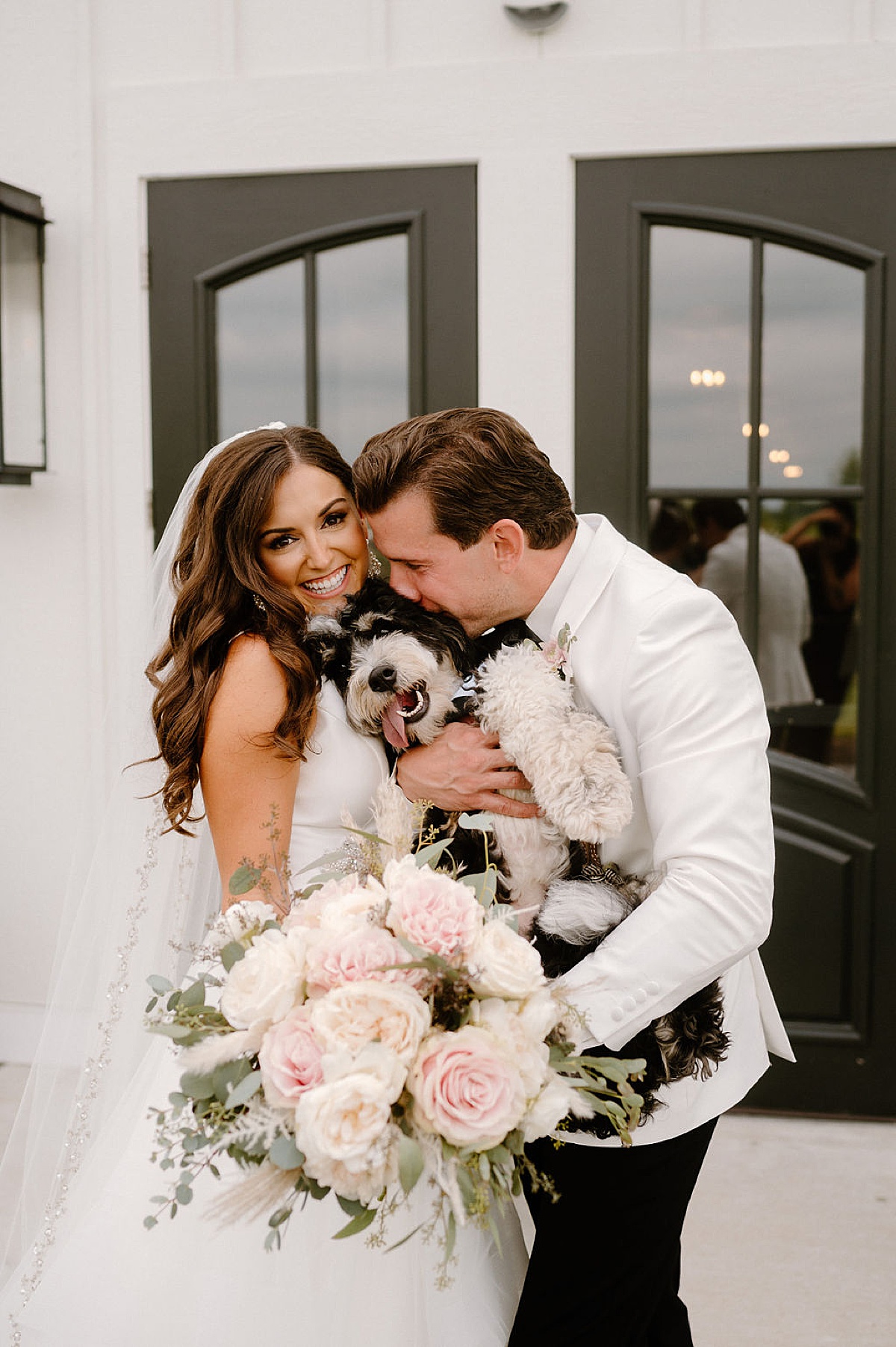 bride with pale pink and white rose bouquet cuddles puppy with groom in white jacket during romantic Etre Farms summer wedding