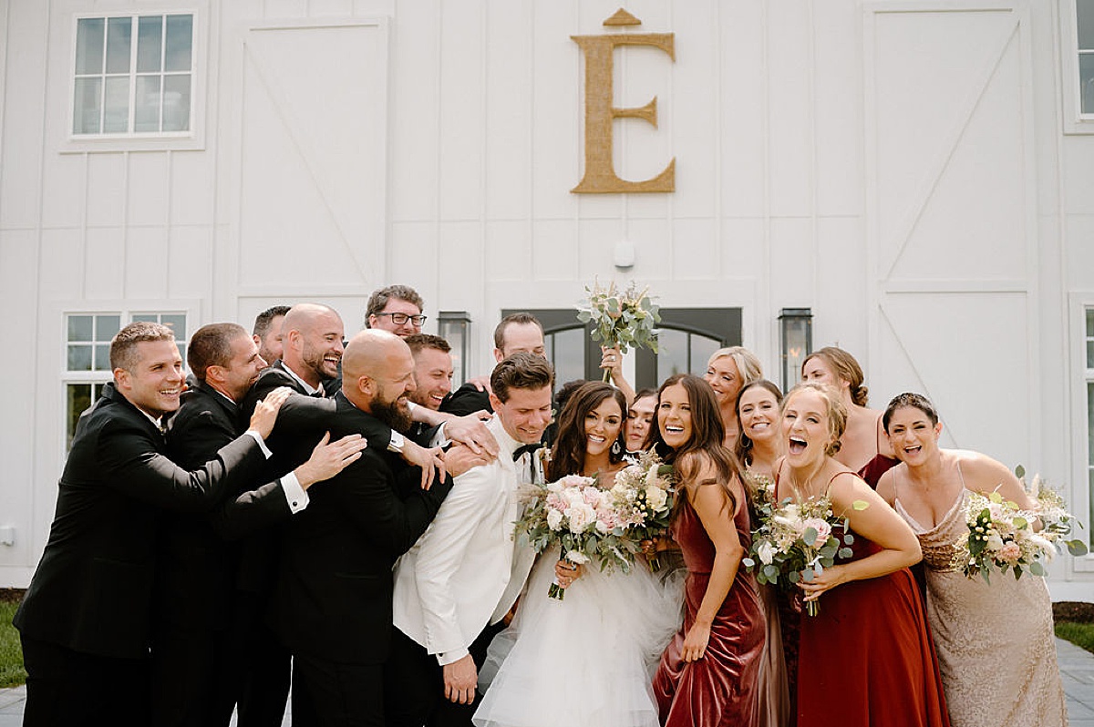 bride and groom are hugged and celebrated by wedding party at modern barn wedding shot by Indigo Lace Collective