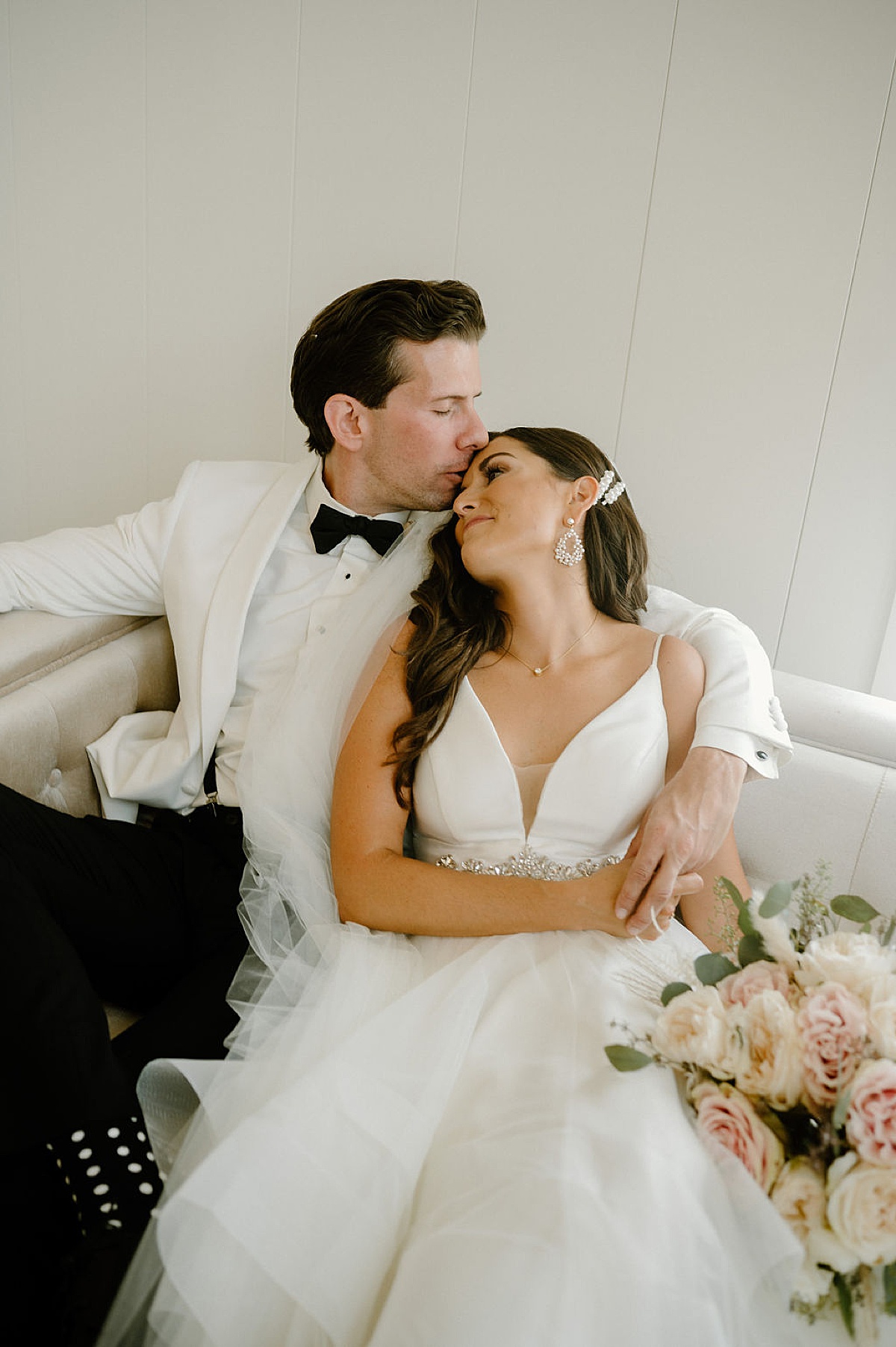elegant bride and groom lounge on white leather couch at modern venue ceremony shot by Indigo Lace Collective