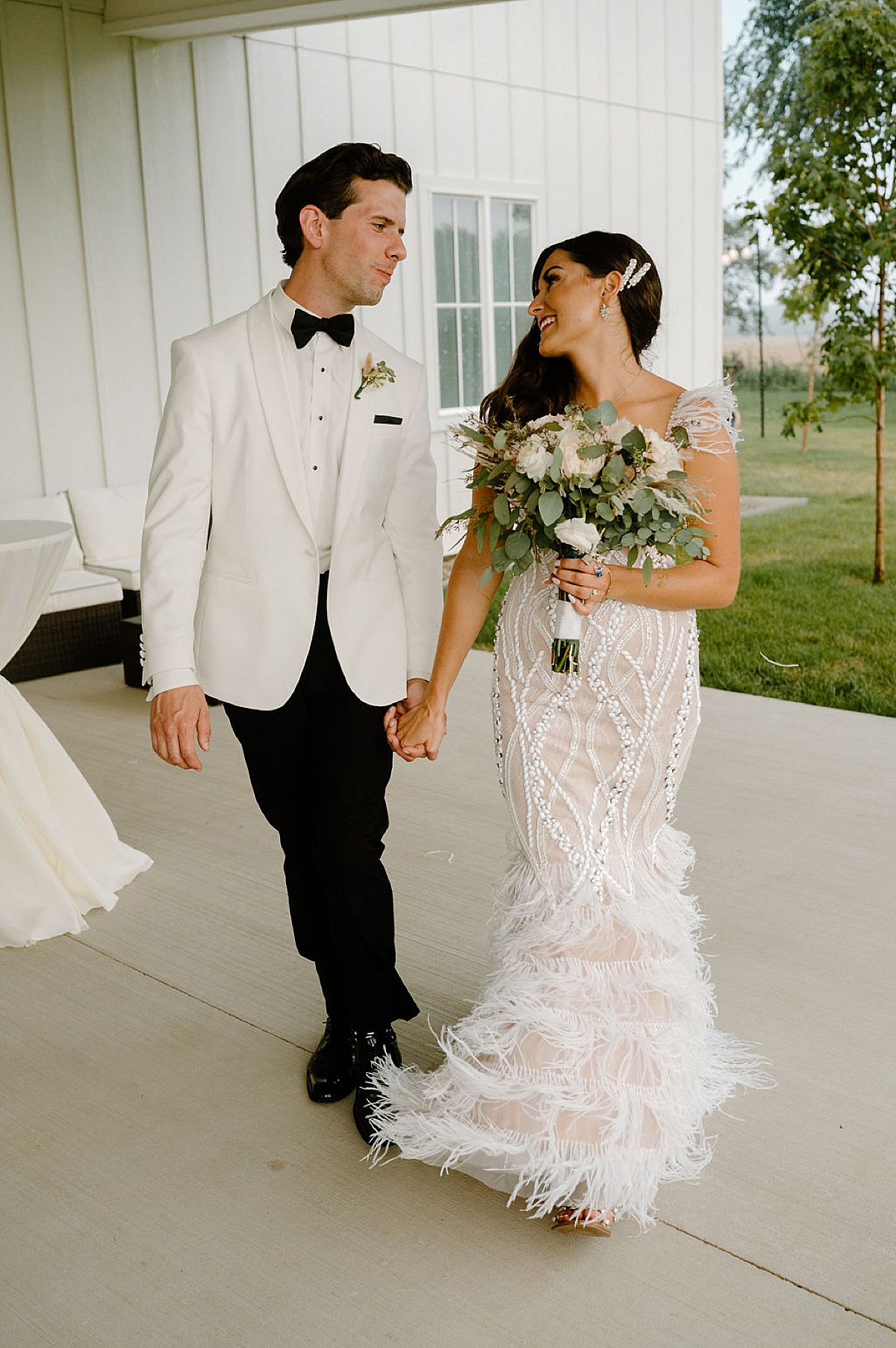 bride in beaded reception dress with feather trim poses with groom in white dinner jacket at reception shot by Michigan wedding photographer