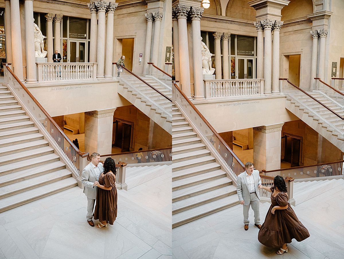 cute romantic couple twirls and dances on grand staircase during Flirty art institute engagement shoot