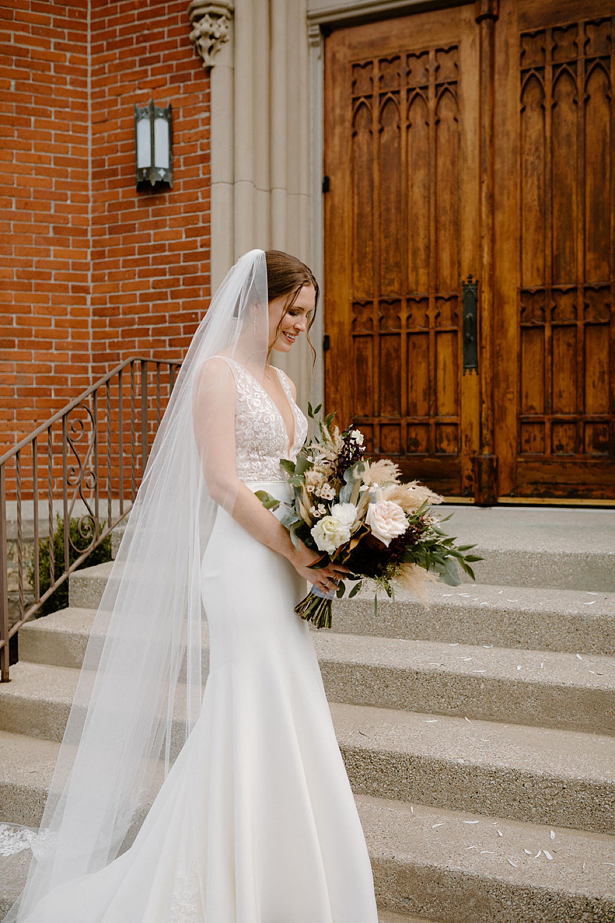 bride in boho sheer lace v neck wedding gown holds pampas grass and rose bouquet during shoot with midwest wedding photographer