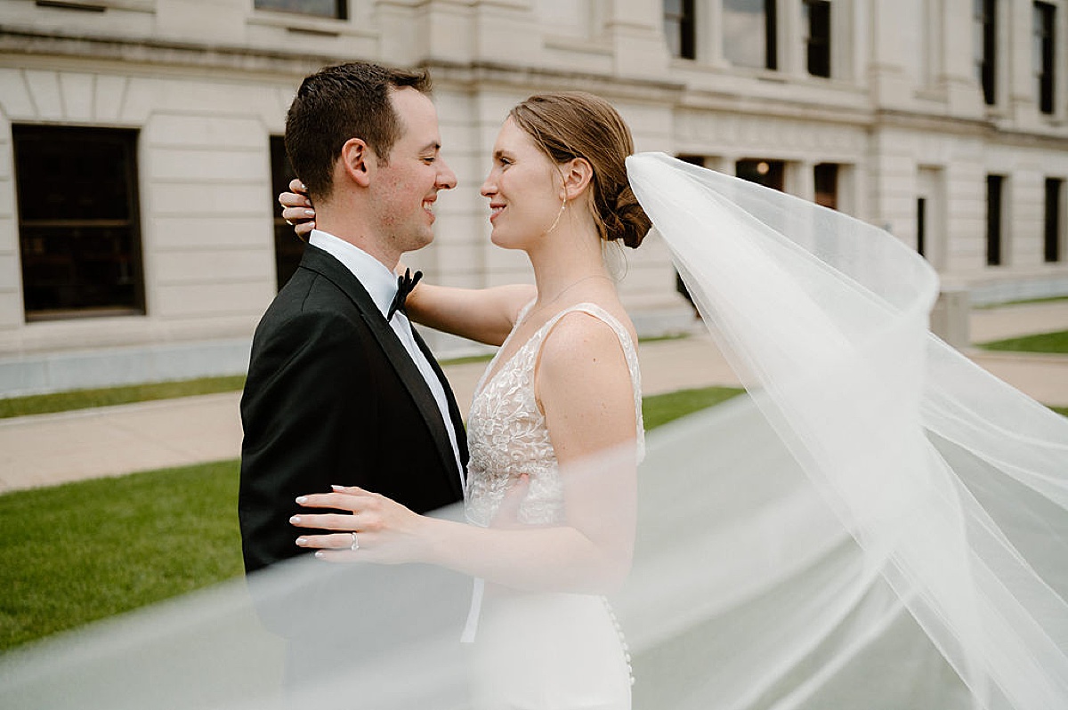 bride's veil floats on the wind as she embraces her groom during session with Indigo Lace Collective