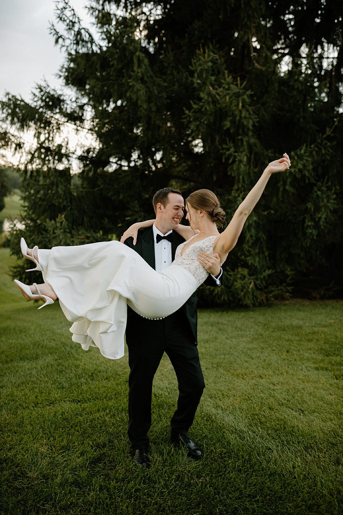 groom sweeps bride off her feet at grassy reception site after wedding ceremony shot by Indigo Lace Collective