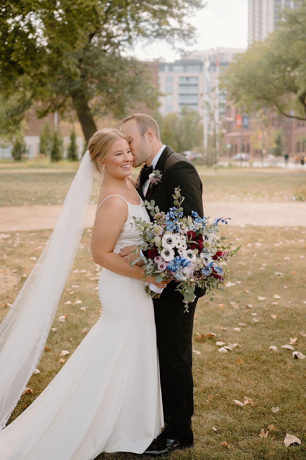 happy bride and groom kiss in autumn park with colorful bouquet of wildflowers after intimate Chicago ceremony