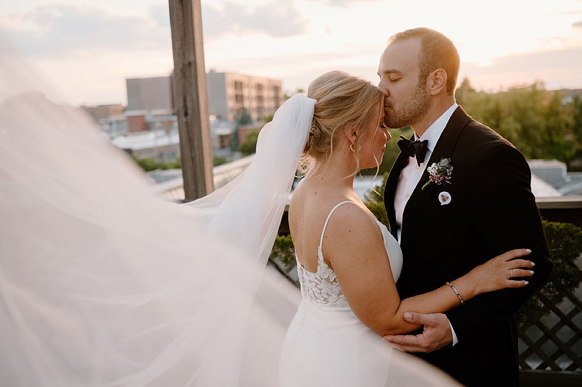 groom kisses bride on the forehead on rooftop at sunset after Chicago ceremony shot by Indigo Lace Collective