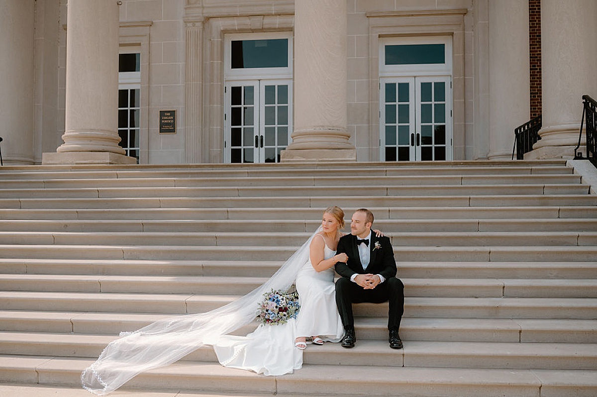 bride with long veil and colorful bouquet poses with groom on Chicago steps during portraits shot by midwest wedding photographer