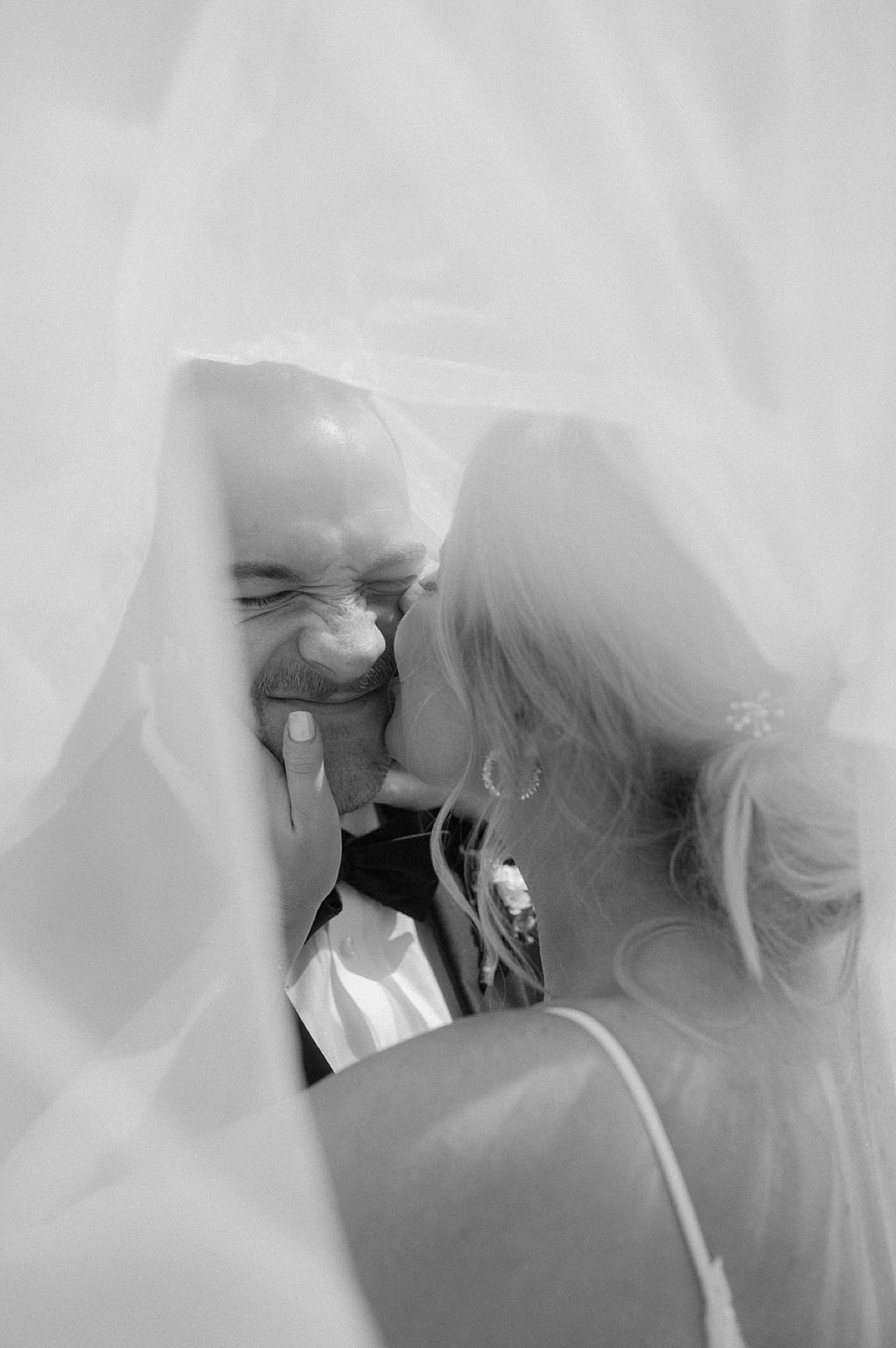 bride kisses groom on the cheek while they pose under her veil after sweet ceremony shot by midwest wedding photographer