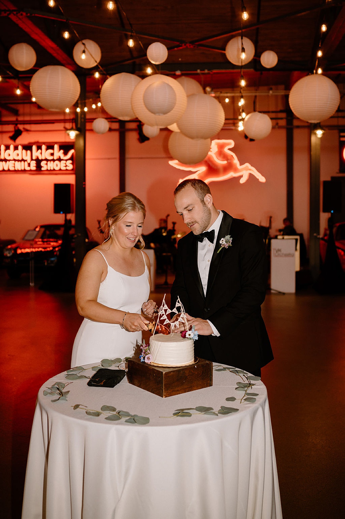 bride and groom cut the cake at unique Chicago reception venue with neon lights shot by midwest wedding photographer