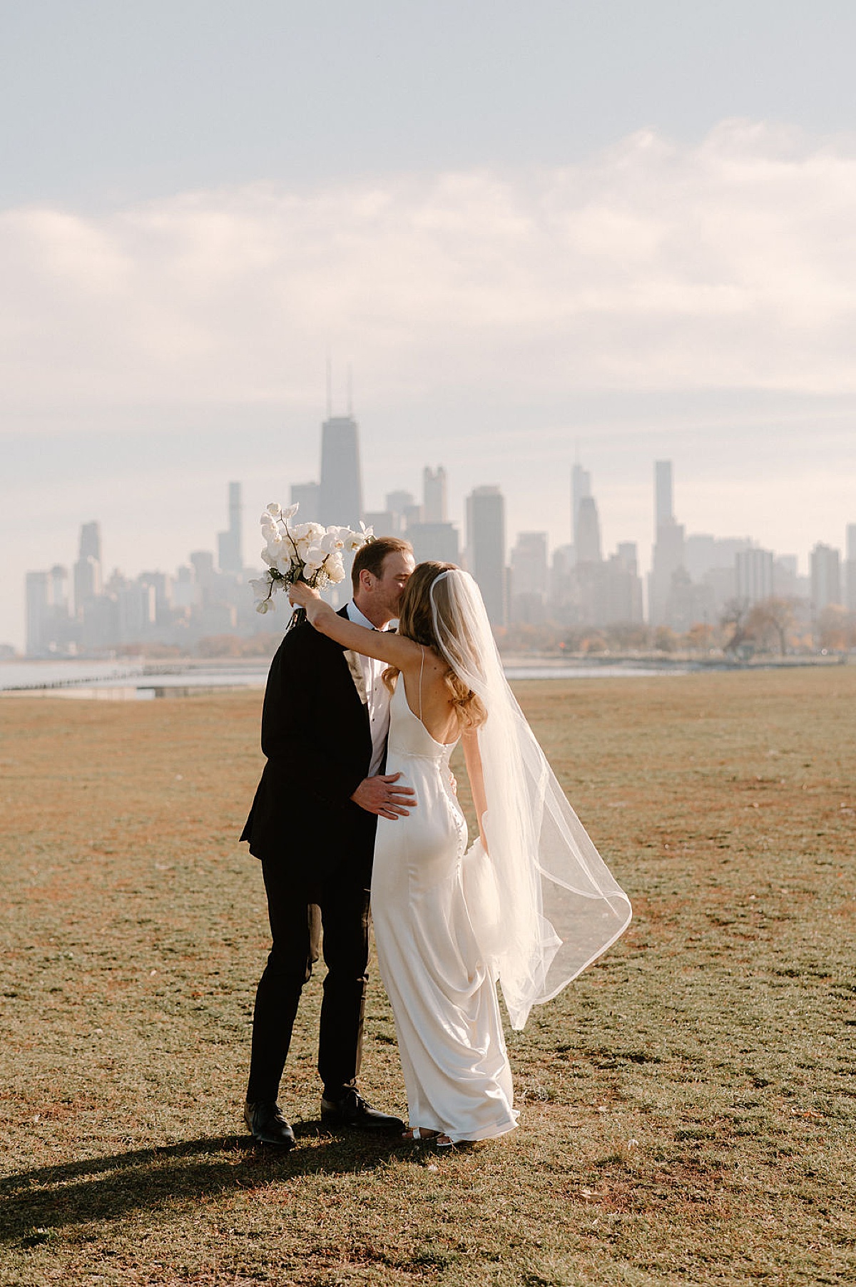 bride with white orchid bouquet poses on the city waterfront with groom before elegant wedding shot by Indigo Lace Collective