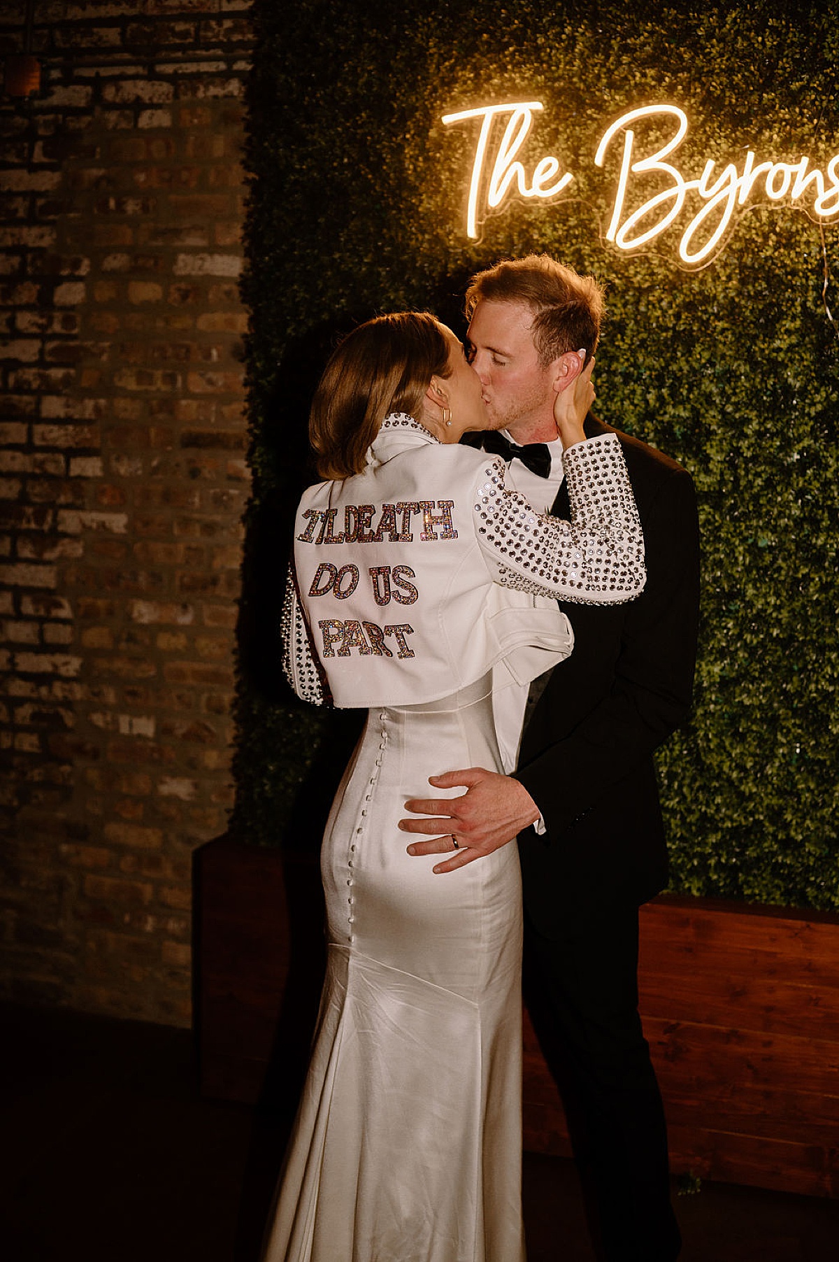bride wearing rock and roll jacket saying 'til death do us part' kisses the groom after reception shot by Chicago wedding photographer
