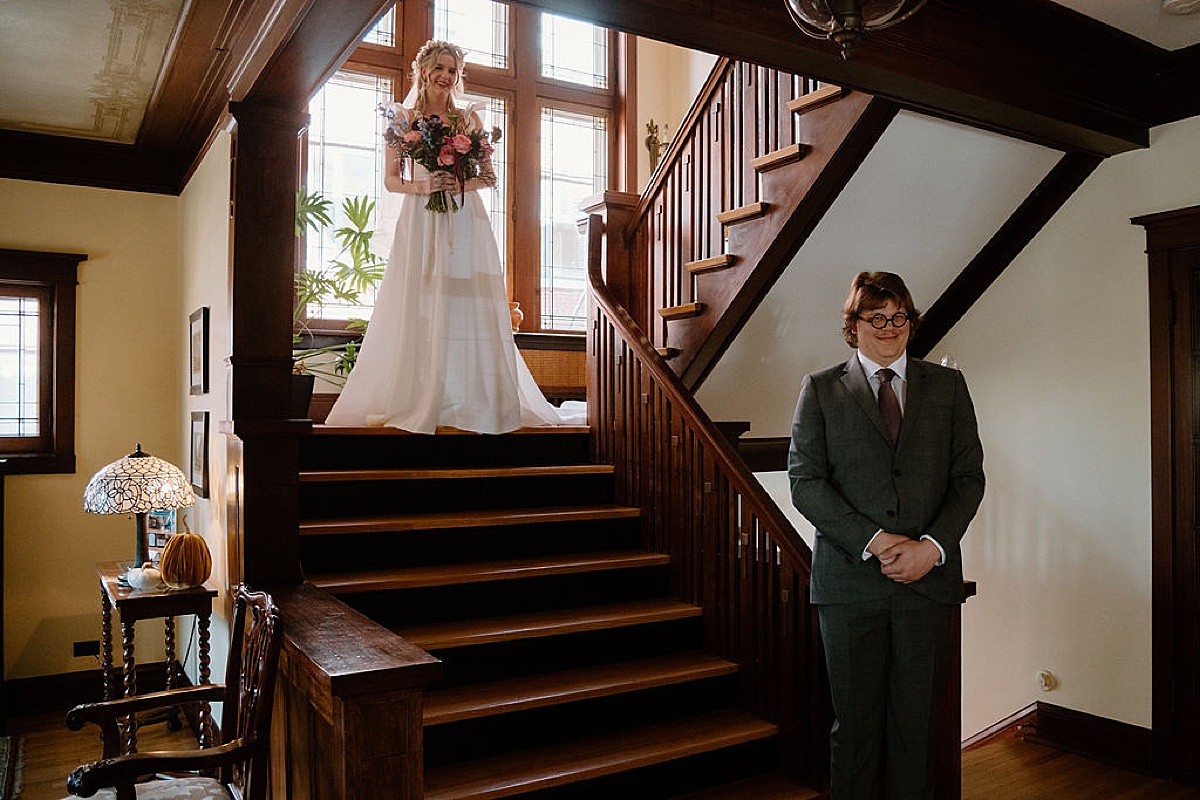 groom waits while bride comes down the stairs for first look before elegant celebration at Frank Lloyd Wright house