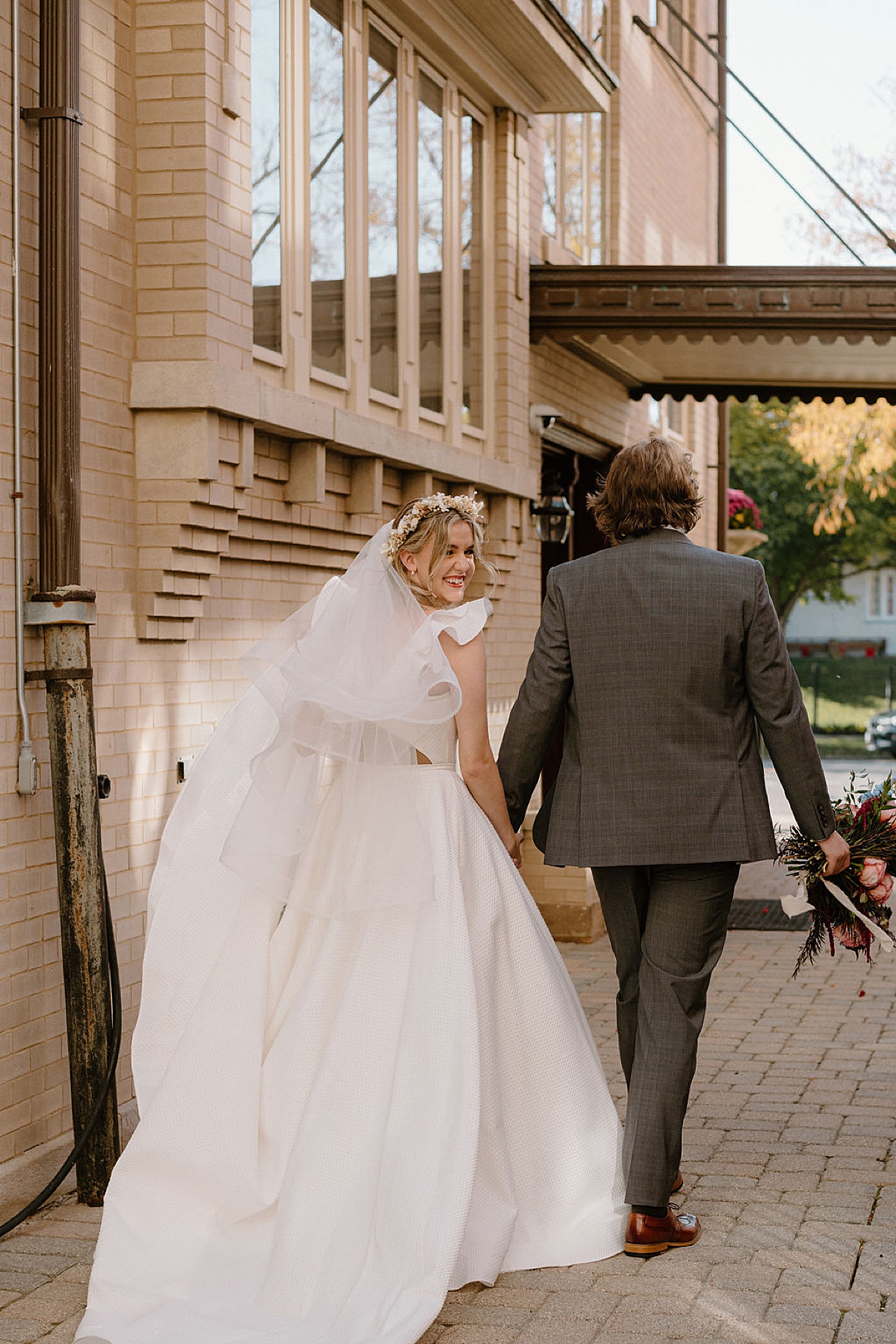 bride in whimsical veil and gown walks hand in hand with groom before ceremony shot by chicago wedding photographer