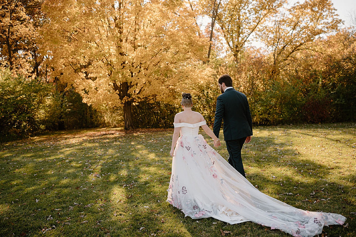 newlywed husband and wife walk into the sunset after romantic autumn arboretum wedding