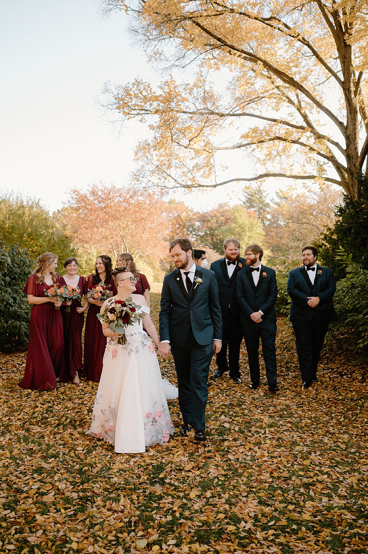 wedding party in burgundy and midnight blue walk behind bride and groom during shoot with Indigo Lace Collective