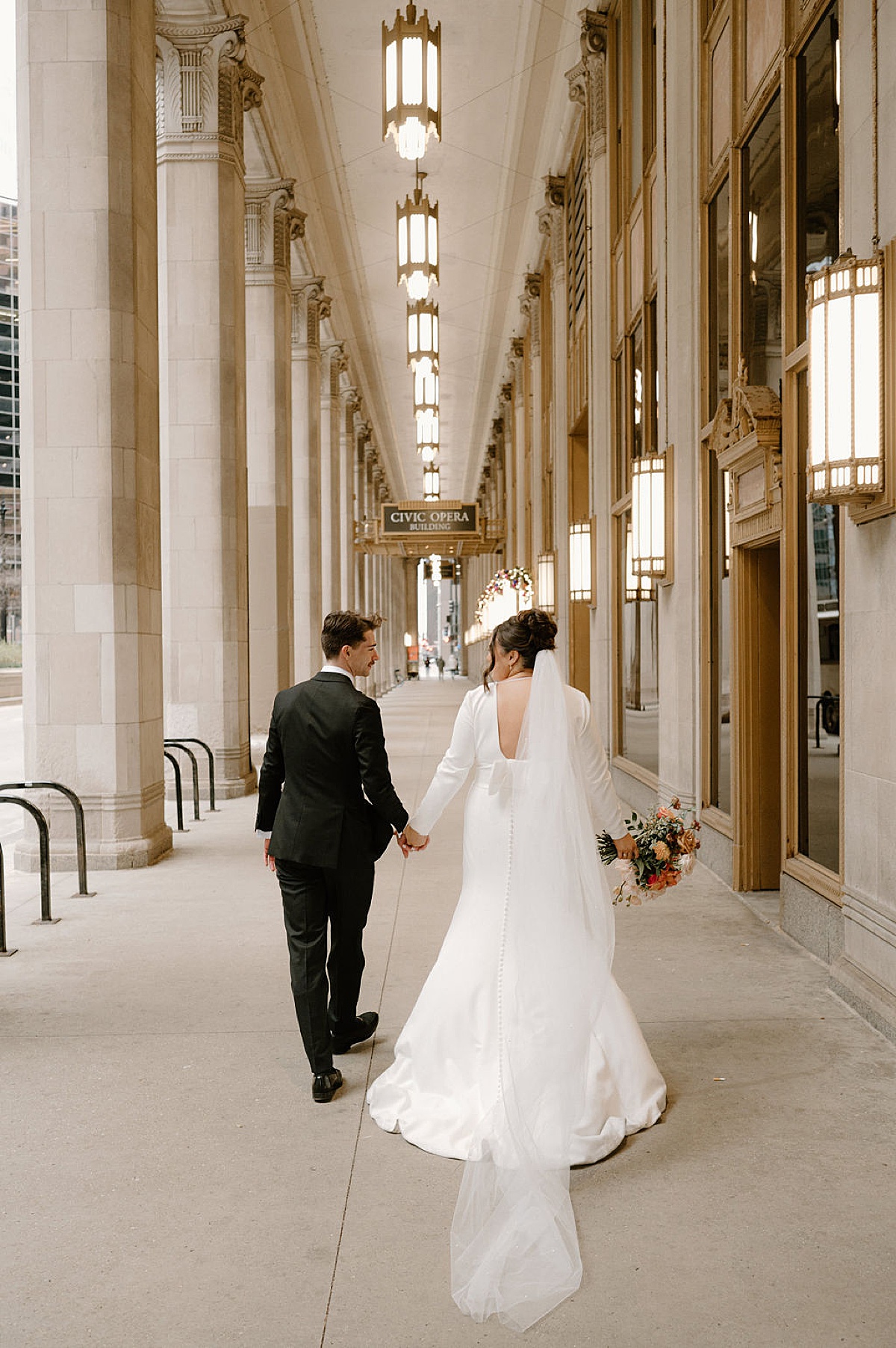 elegant bride and groom walk in front of civic opera house before glam reception shot by Chicago wedding photographer
