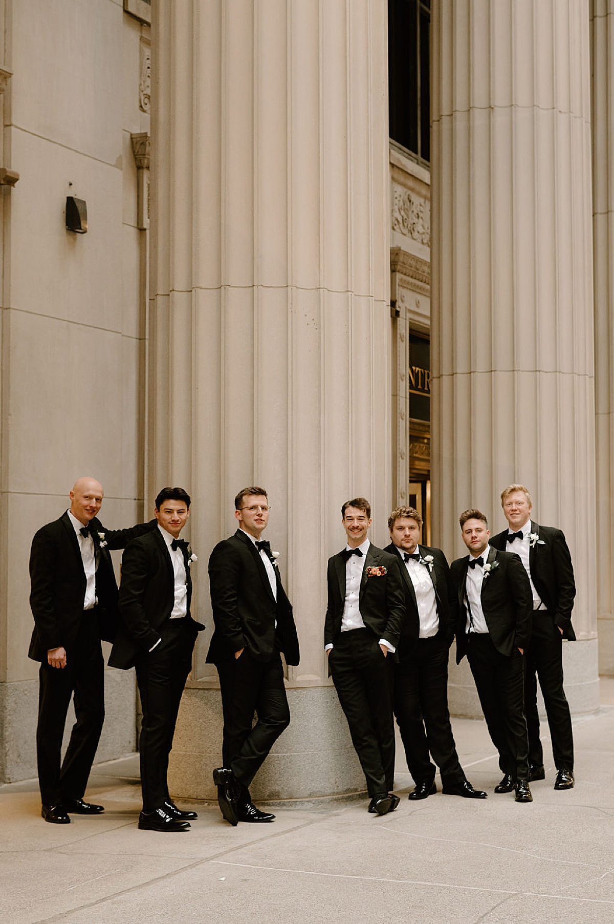 groomsmen pose by giant stately columns before ceremony shot by Chicago wedding photographer