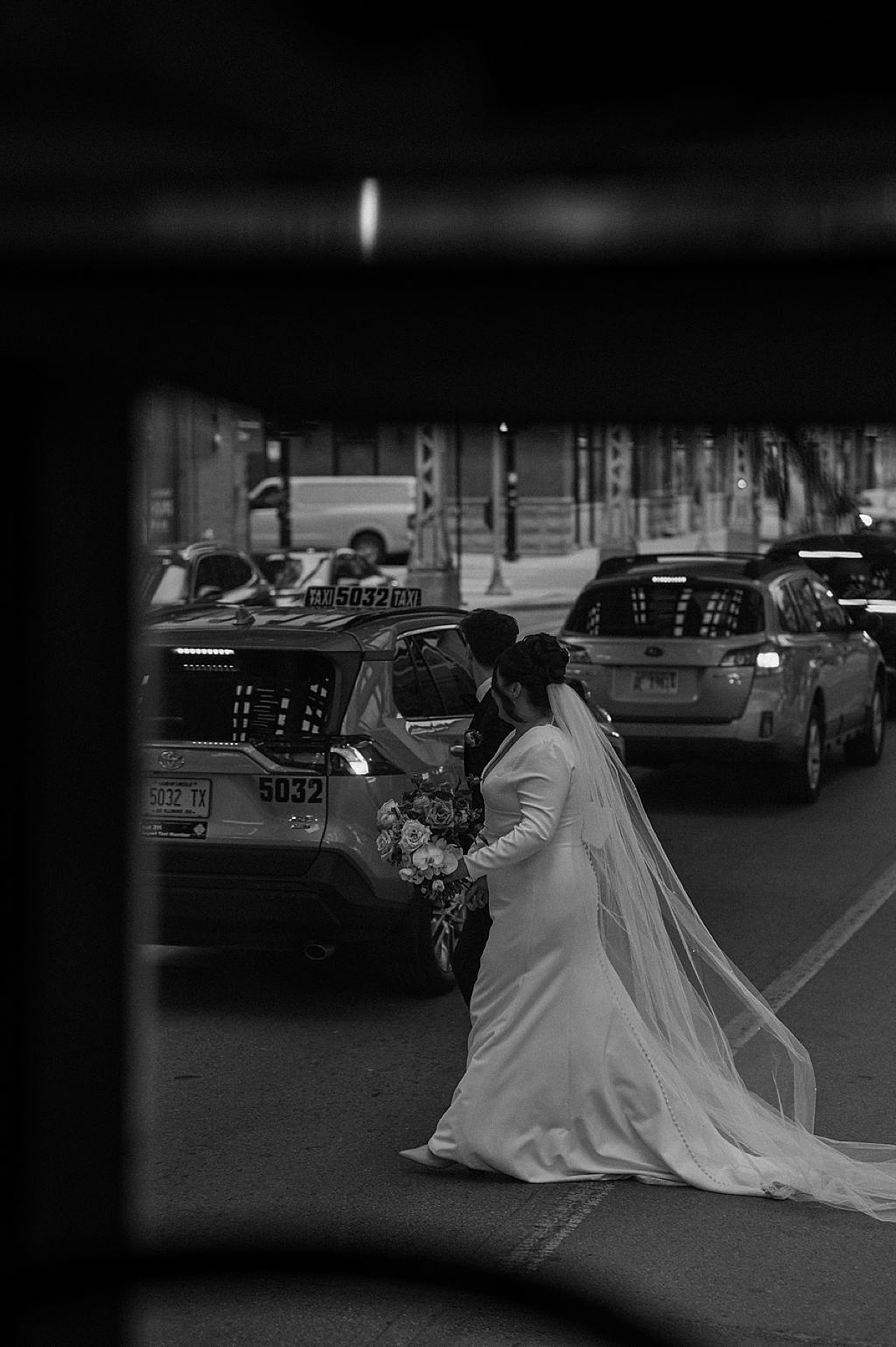 bride in simple elegant gown holds hands with groom as they cross busy chicago street shot by Indigo Lace Collective