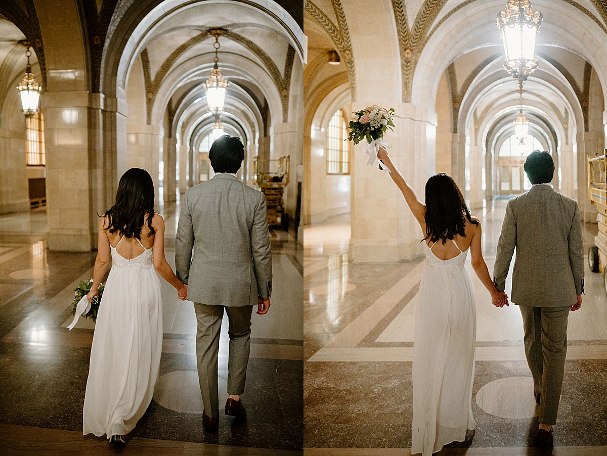 groom in gray suit and bride in delicate gown walk hand in hand through marble hallway during city hall sweetheart elopement