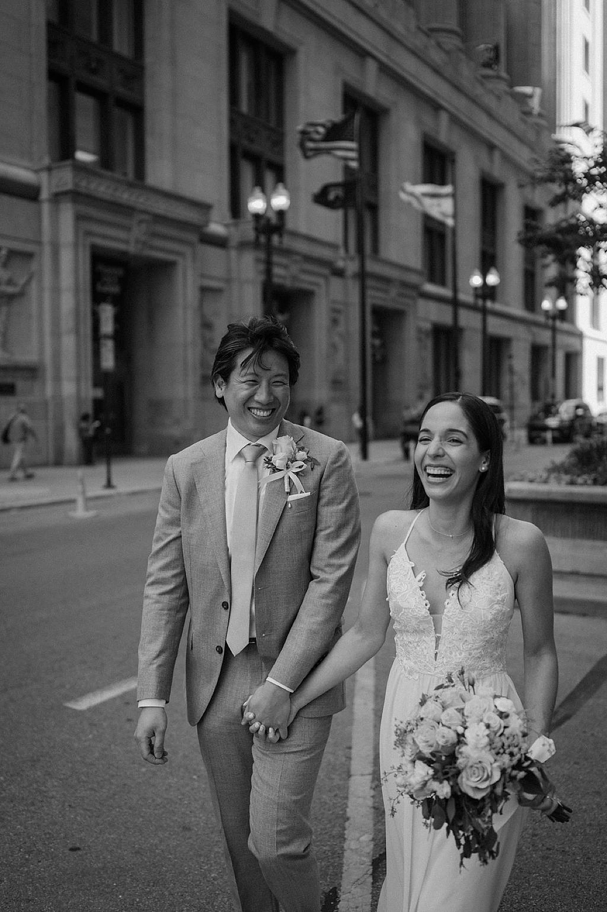 grinning bride and groom in dapper suit and delicate gown walk down Chicago street after city hall sweetheart elopement