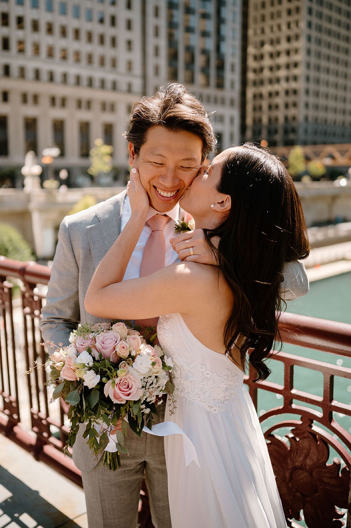 sweet bride kisses her groom on the cheek as they pose over the river shot by Chicago wedding photographer