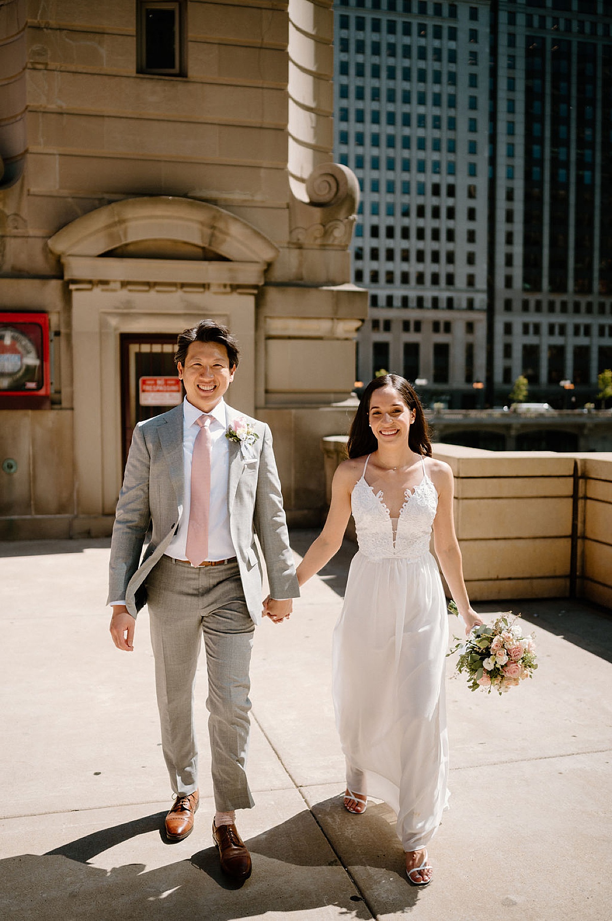 bride in pretty gown and groom in dapper suit walk hand in hand during photos shot by Chicago wedding photographer