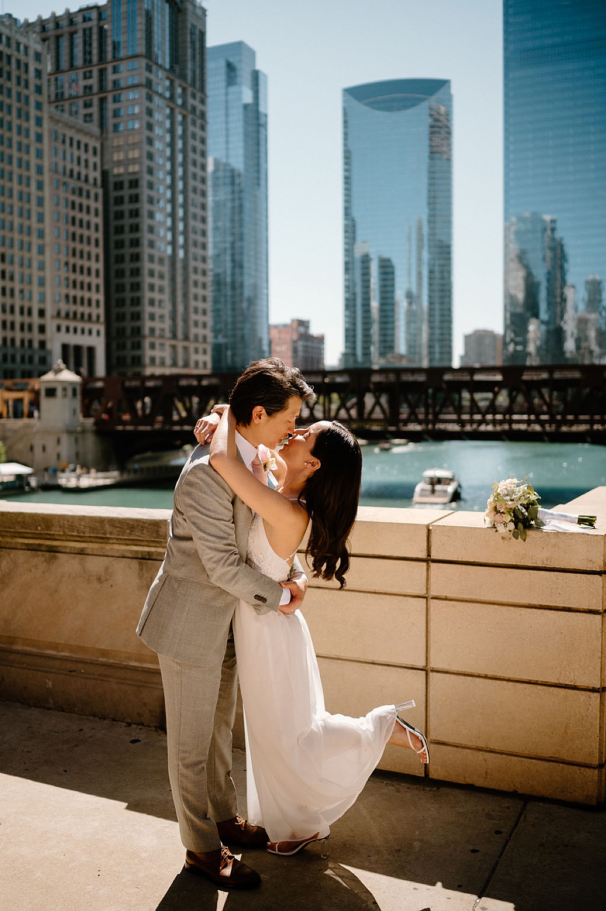 bride and groom in dapper summer evening wear kiss on stone bridge over Chicago river shot by Indigo Lace Collective