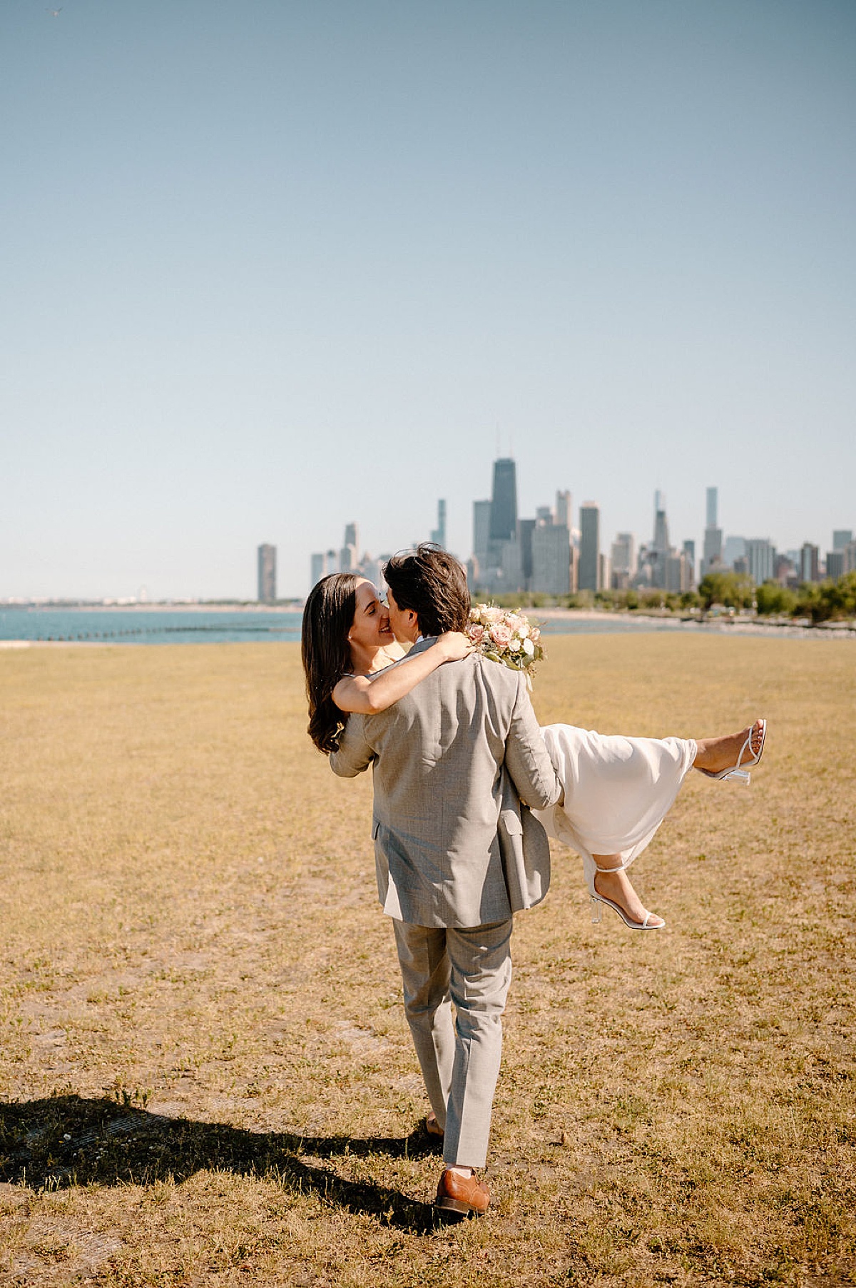 groom in gray suit sweeps bride off her feet with chicago skyline in background | shot by Indigo Lace Collective
