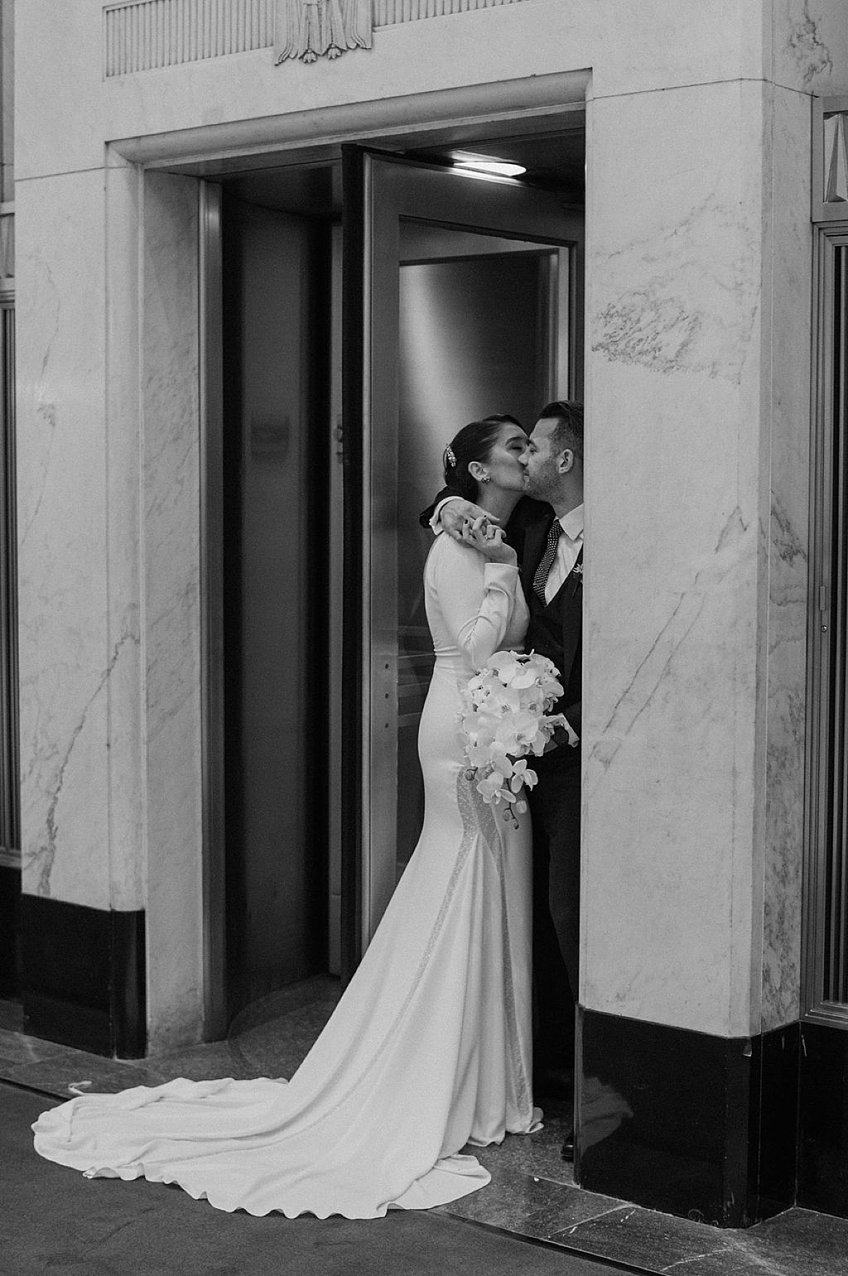 elegant bride with orchid bouquet kisses groom outside gold doors during celebration at old Chicago post office