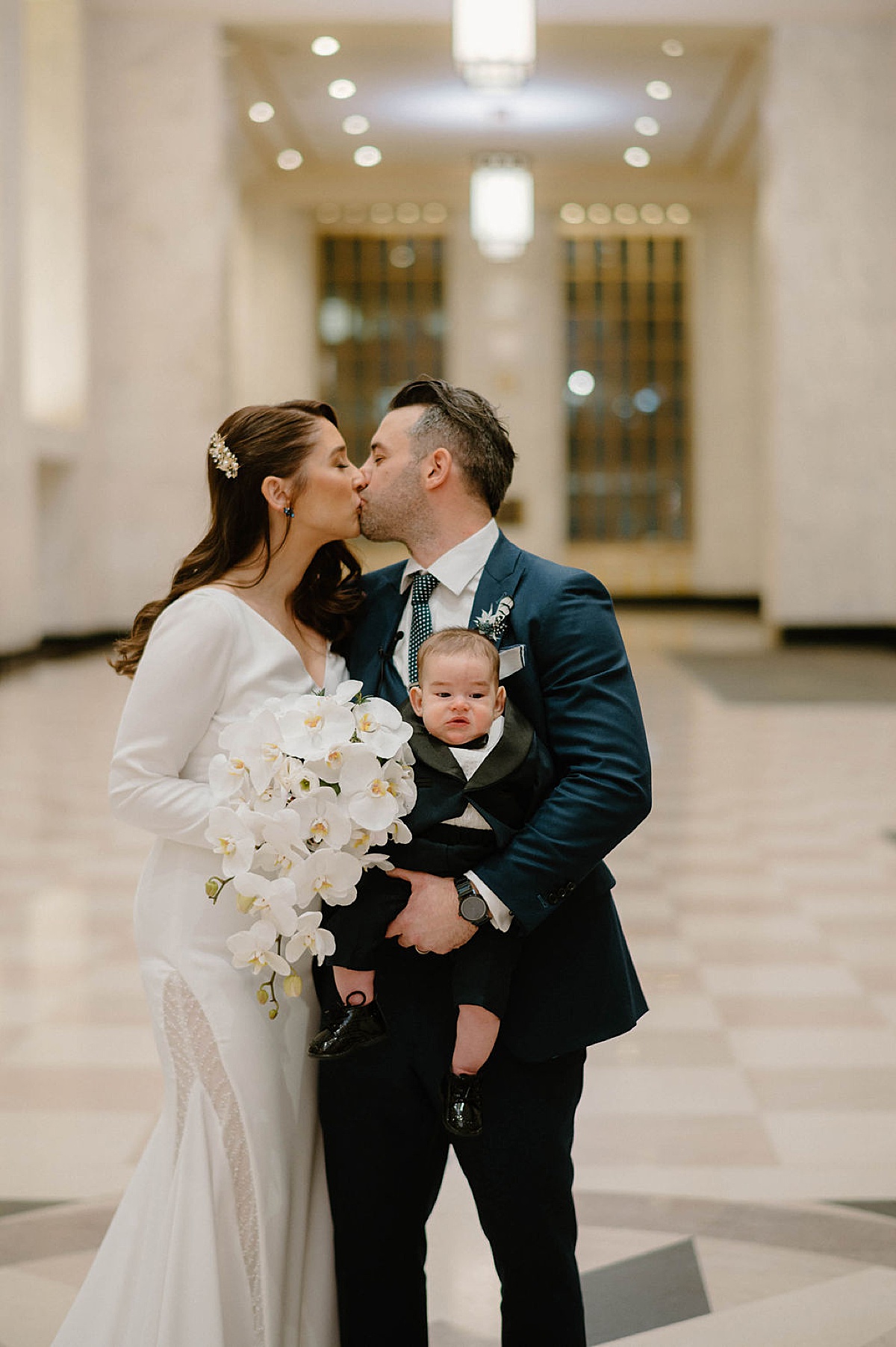 bride and groom hold baby boy and kiss after post elopement celebration shot by Chicago wedding photographer