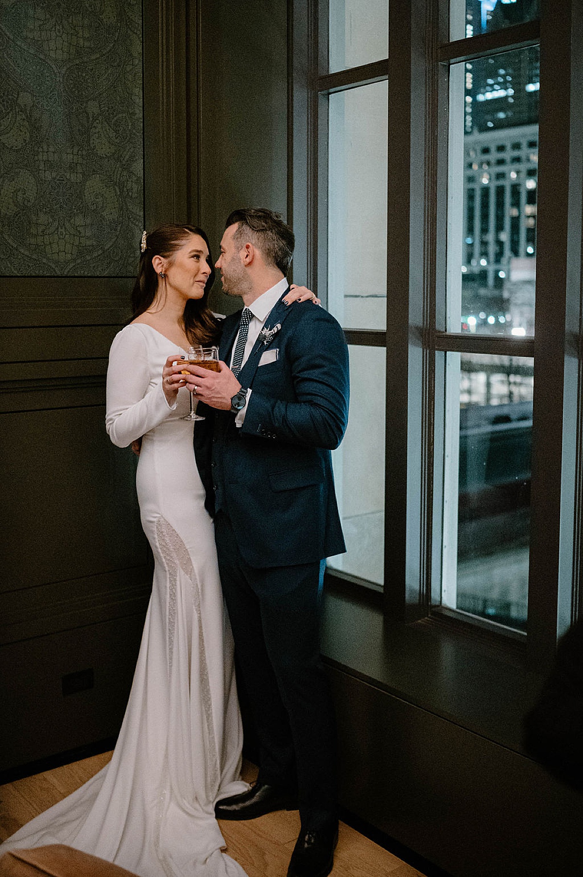 classy christmas bride and groom pose in Chicago high rise window with cocktails after ceremony shot by Indigo Lace Collective