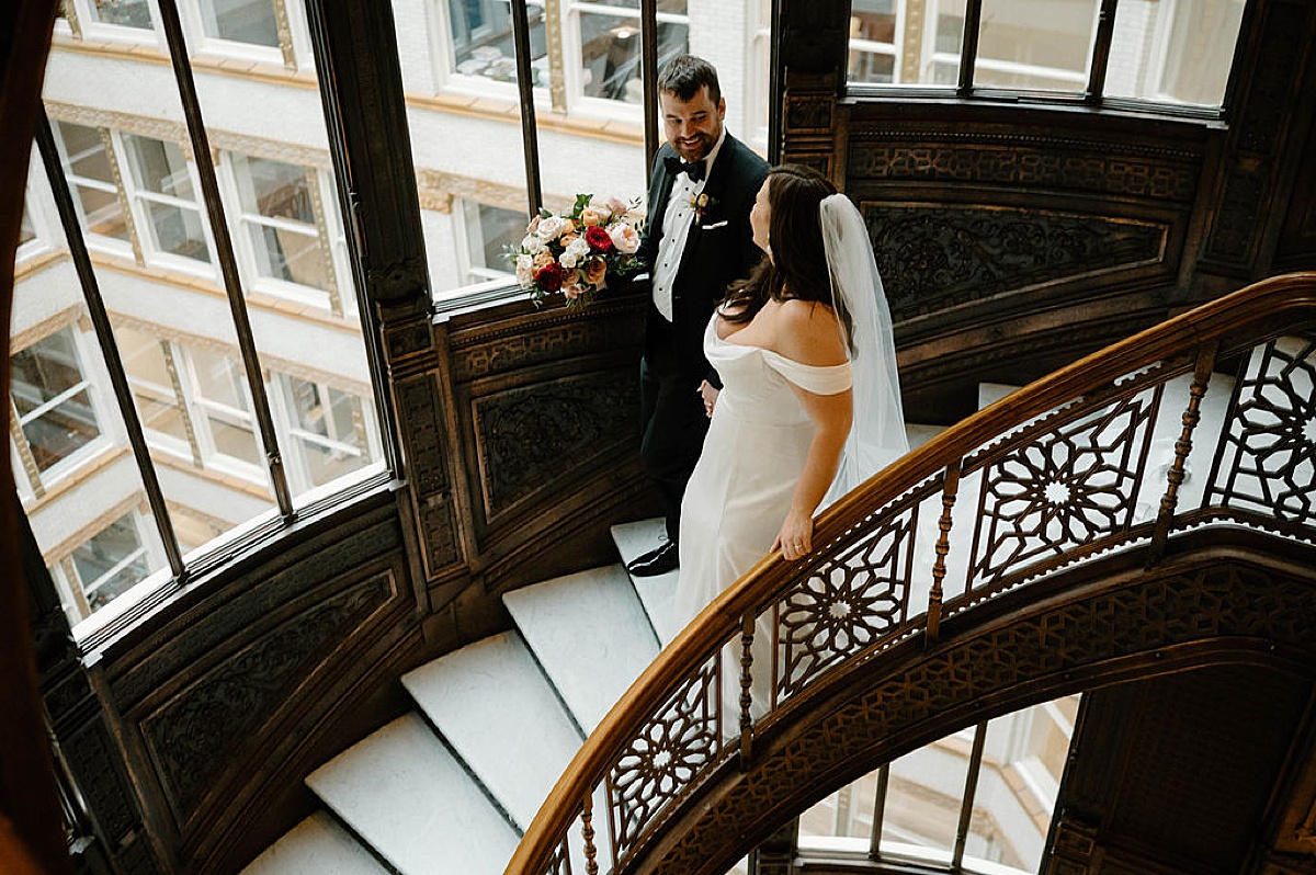 bride and groom walk hand in hand down spiral staircase after romantic winter celebration