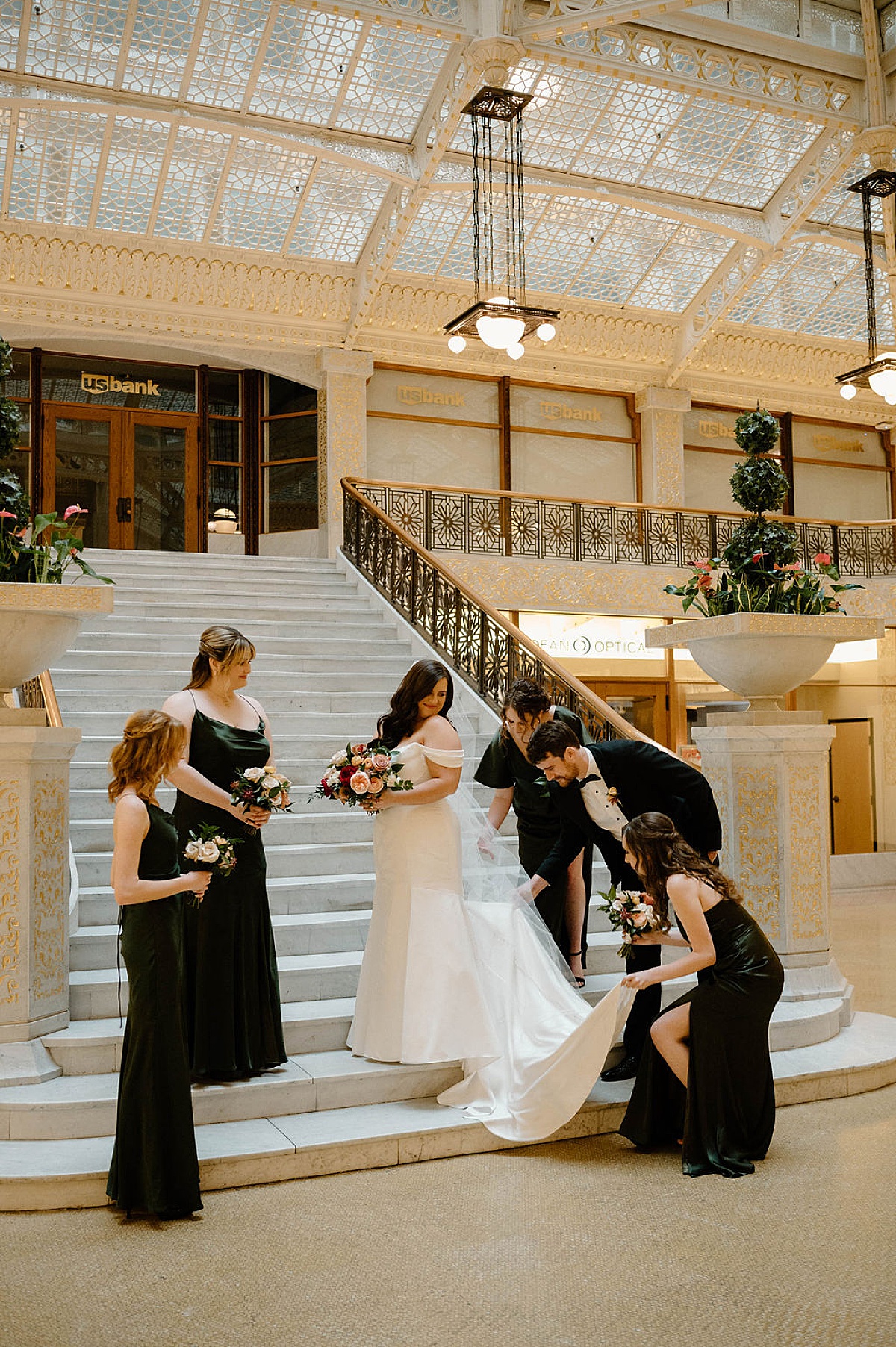 bridal party helps adjust bride's train during classy photos on marble steps shot by Chicago wedding photographer