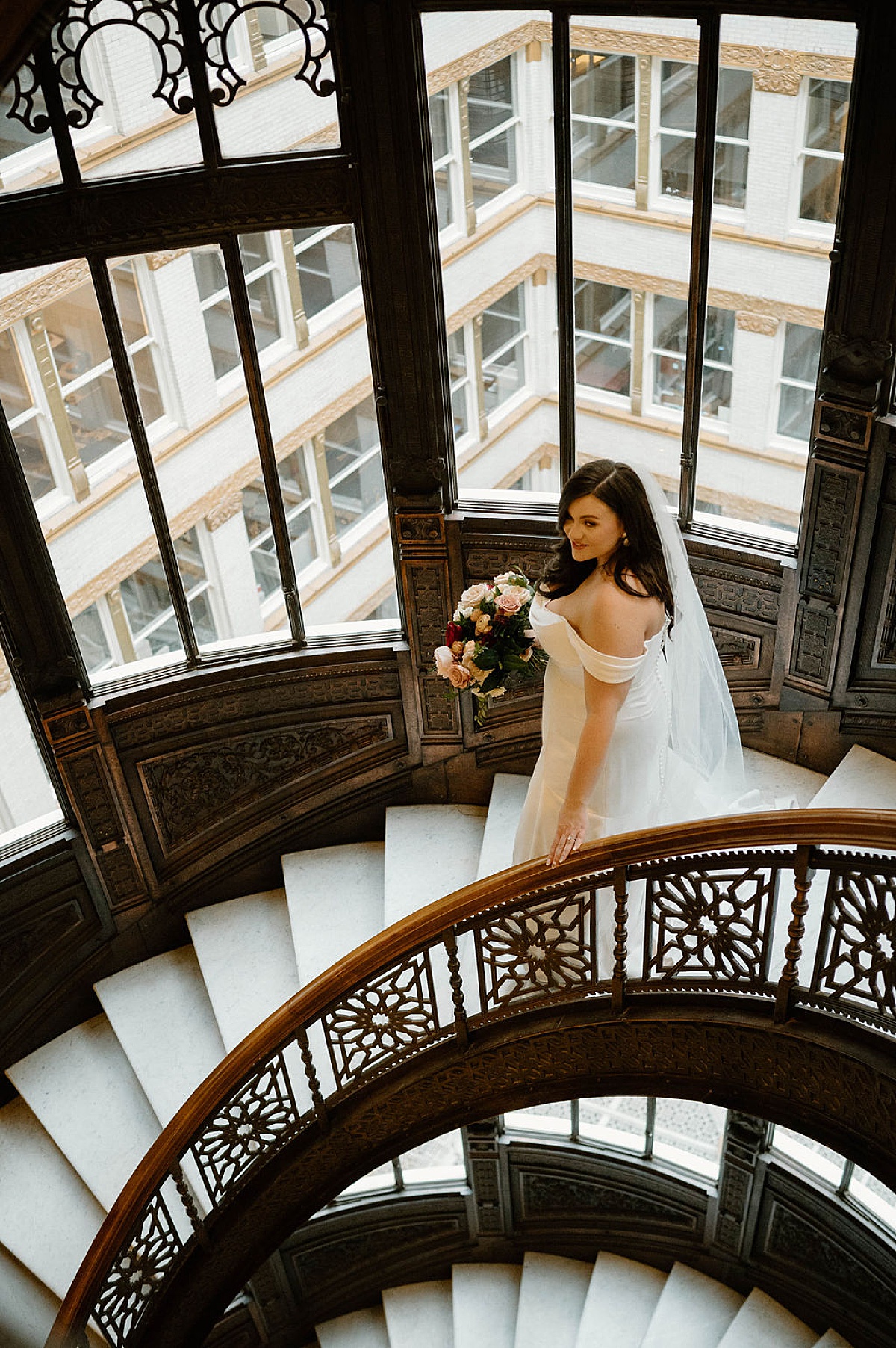 bride poses on circular stairway with windows overlooking Chicago shot by Indigo Lace Collective