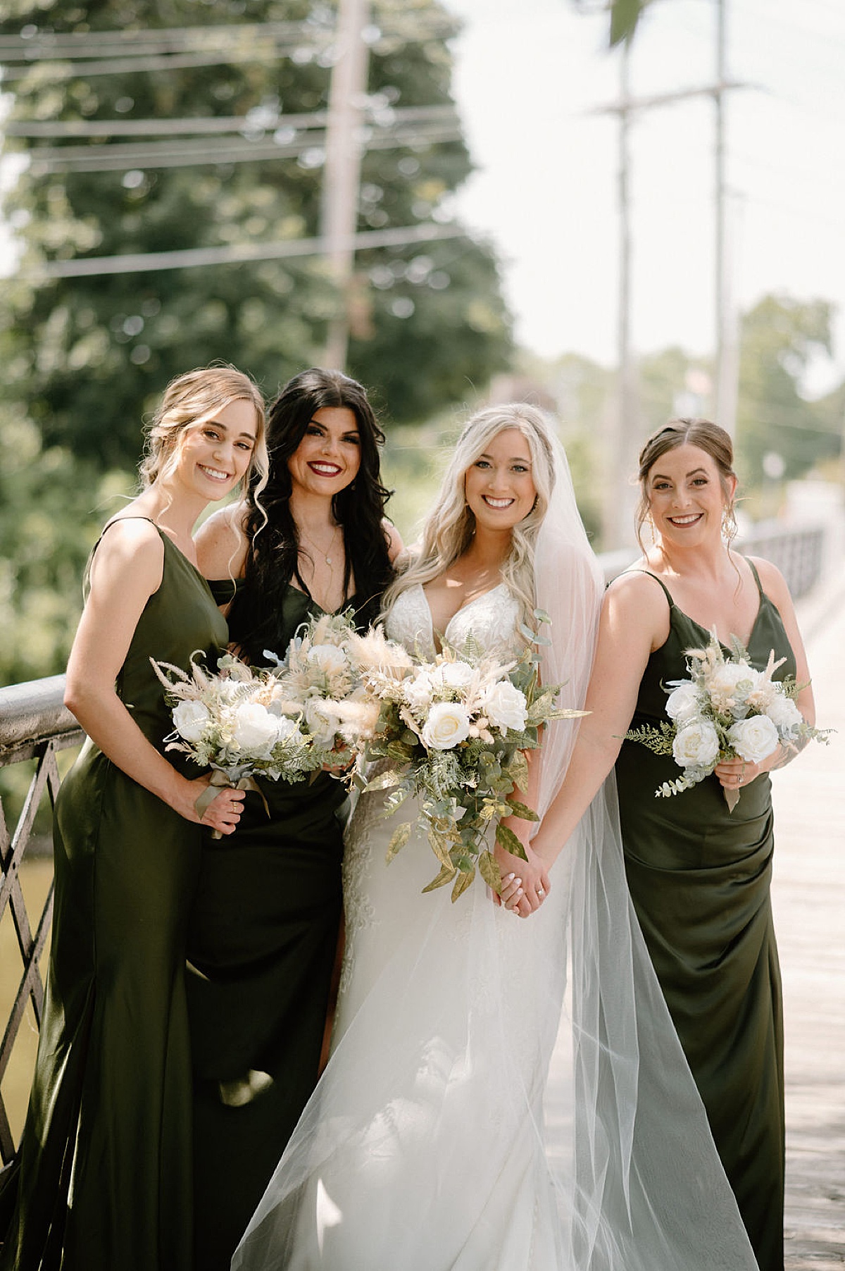 boho classy bride in lace gown and bouquet of roses, eucalyptus, and pampas grass poses with bridesmaids in green gowns shot by Indigo Lace Collective