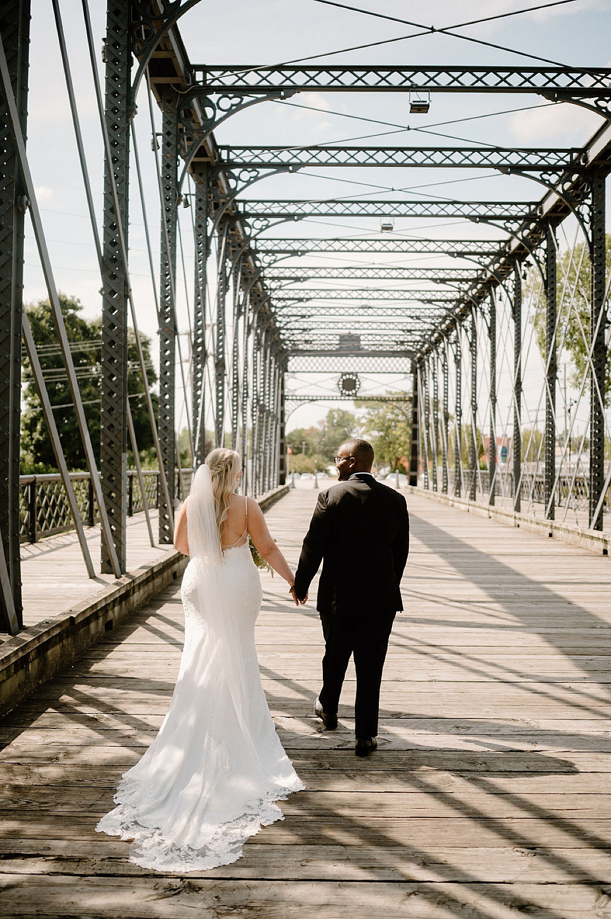 bride and groom walk hand in hand across trestle bridge in fort wayne shot by Indigo Lace Collective